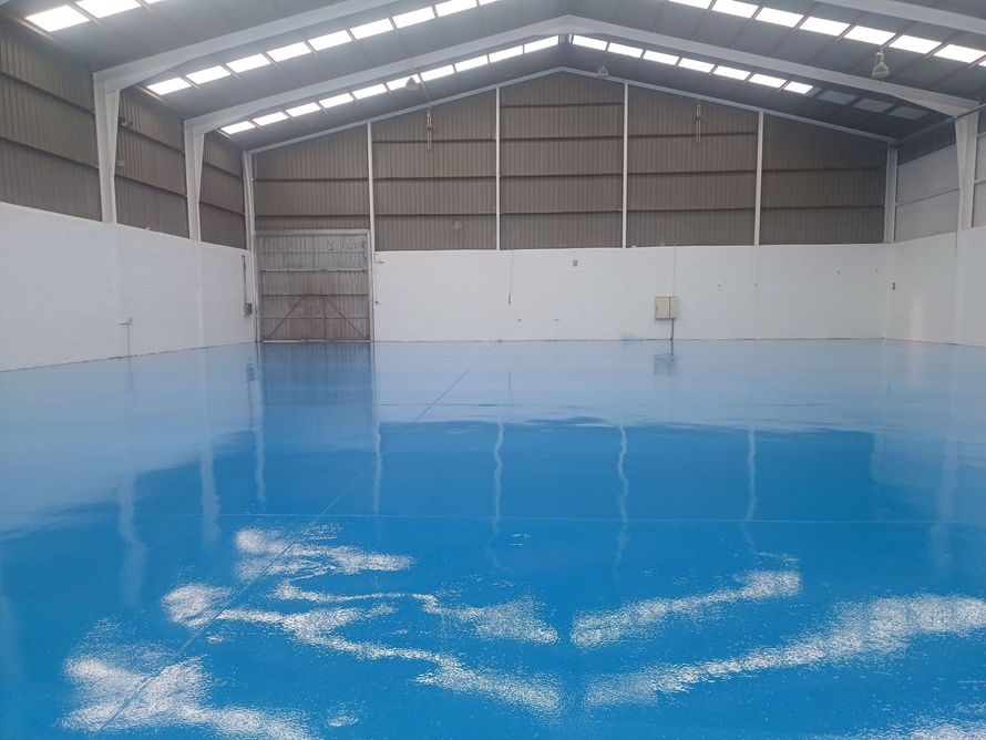 Interior de almacén con suelo azul, paredes blancas y techo de metal.