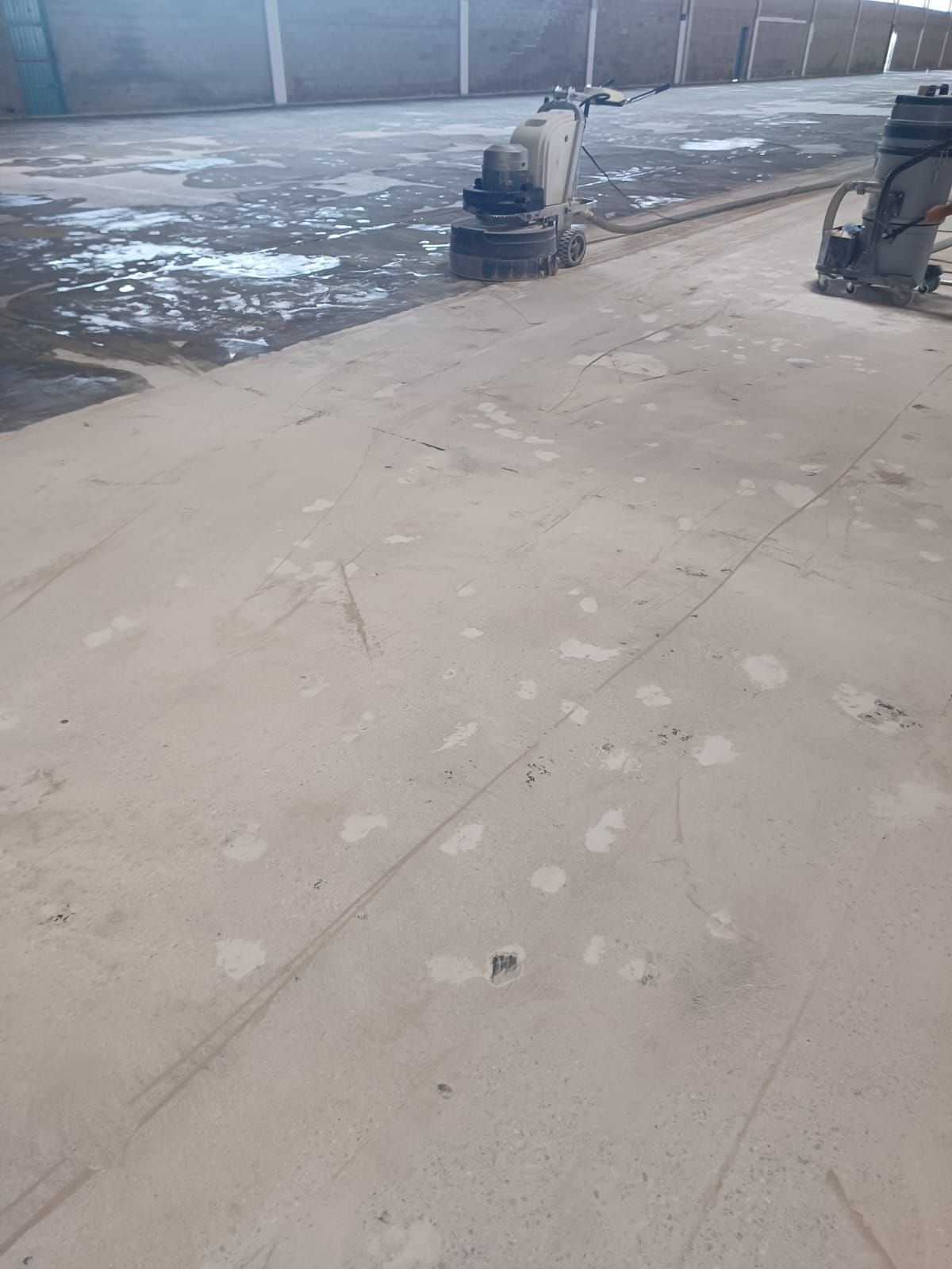 Dos pulidoras de hormigón industriales alisan un suelo de hormigón de color claro en un almacén.