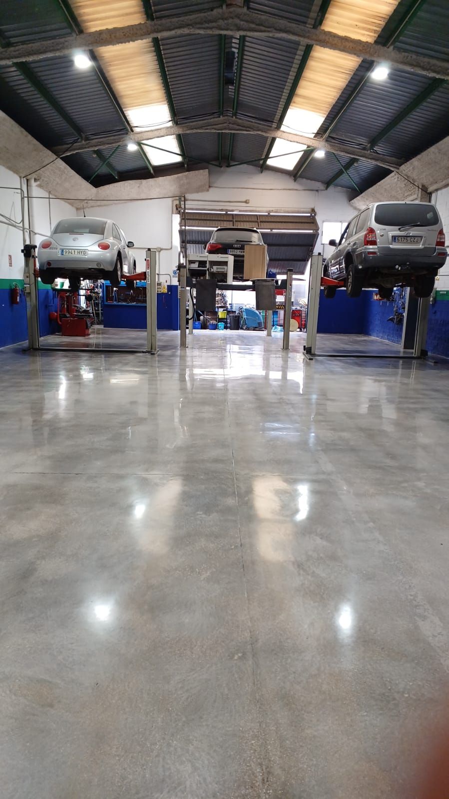 Automóviles en elevadores en un taller de reparación de automóviles bien iluminado, con un piso de concreto reflectante.