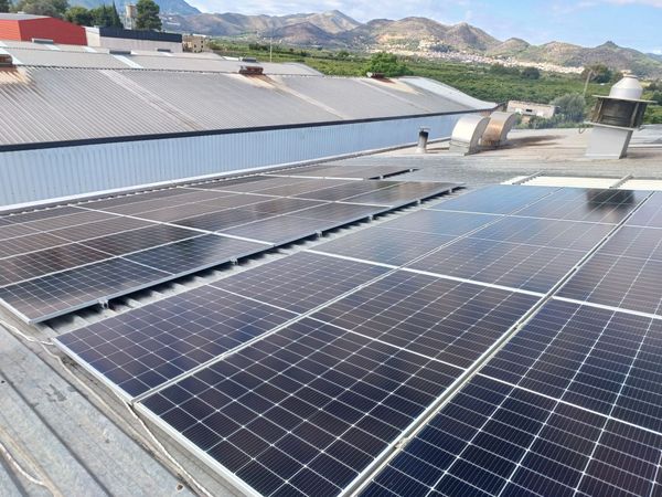 Paneles solares en el techo de un edificio con montañas al fondo bajo un cielo soleado.