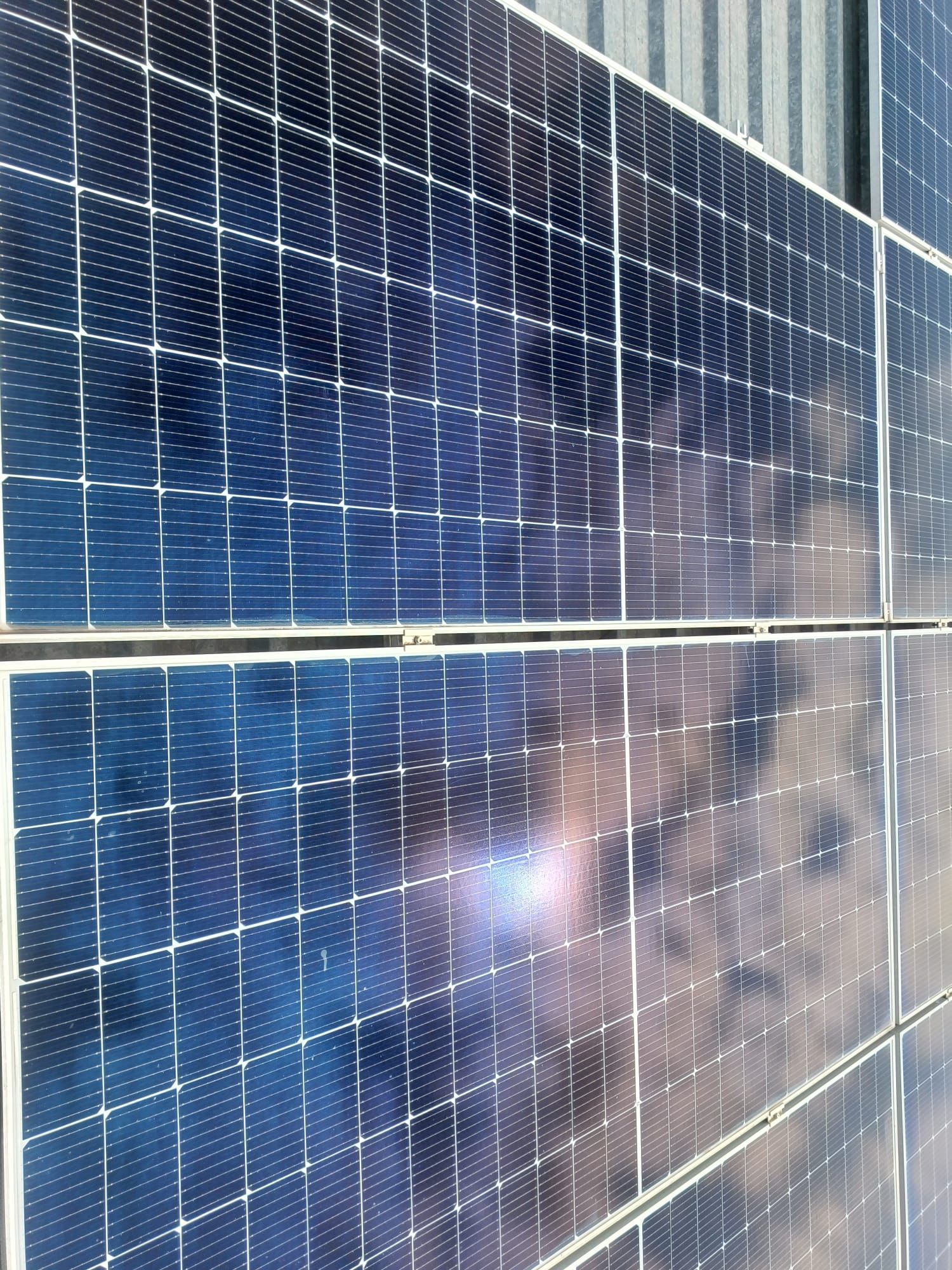 Vista de cerca de paneles solares que reflejan un cielo nublado, dispuestos en un patrón de cuadrícula.