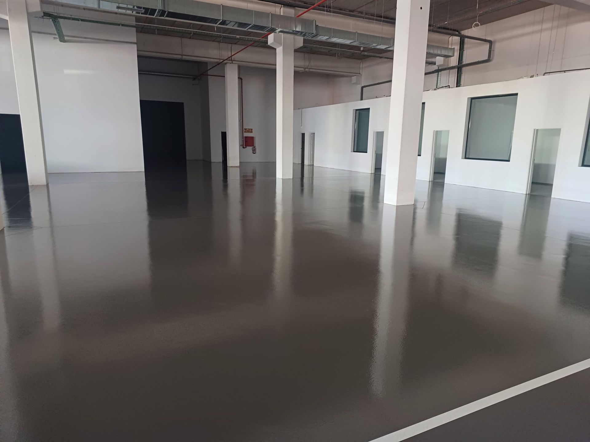 Amplio espacio comercial vacío con suelo gris brillante y columnas y paredes blancas.