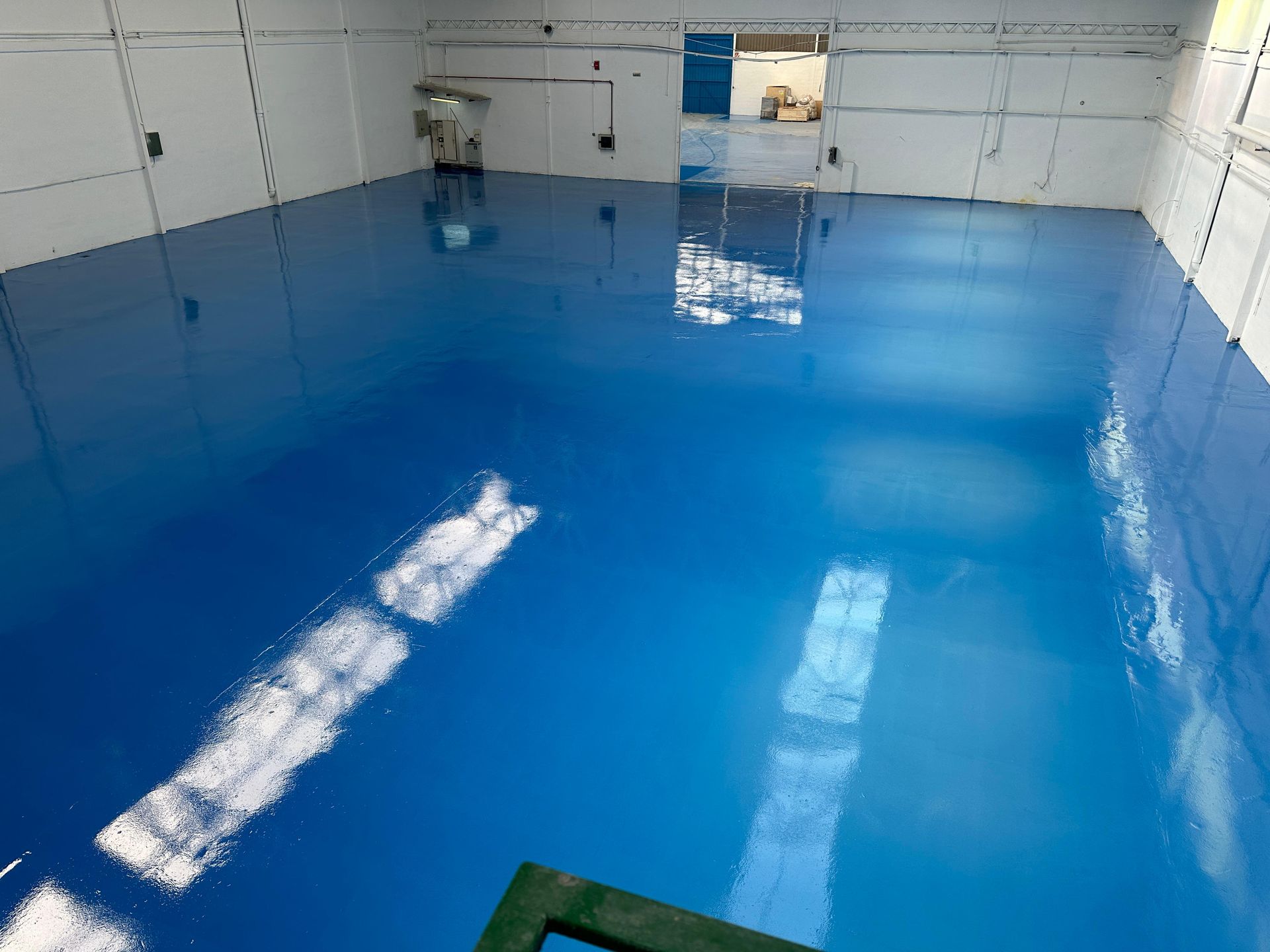 Piso epoxi azul en el interior de un almacén, reflejando la luz y las paredes blancas circundantes.