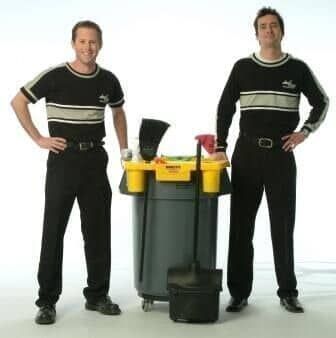 Dois homens de uniforme preto estão ao lado de um carrinho de limpeza.