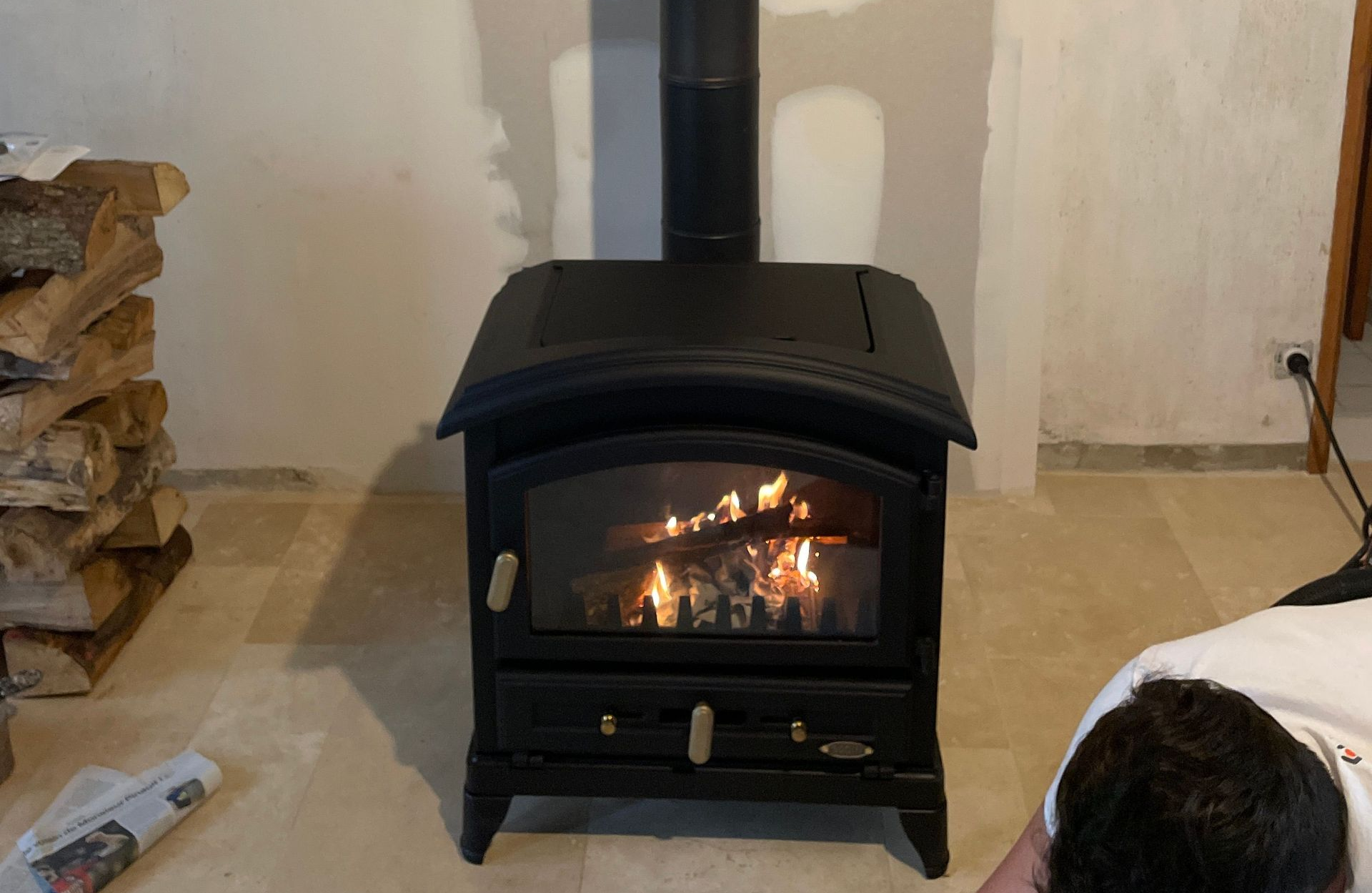 Poêle à bois noir en marche, pile de bûches et chauffagiste