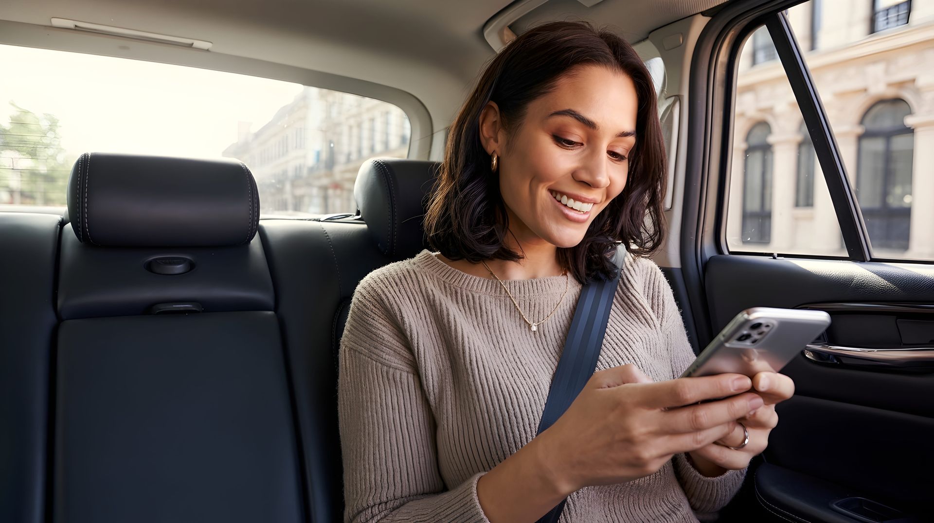 Une femme assise à l'arrière d'une voiture regarde son téléphone en souriant.