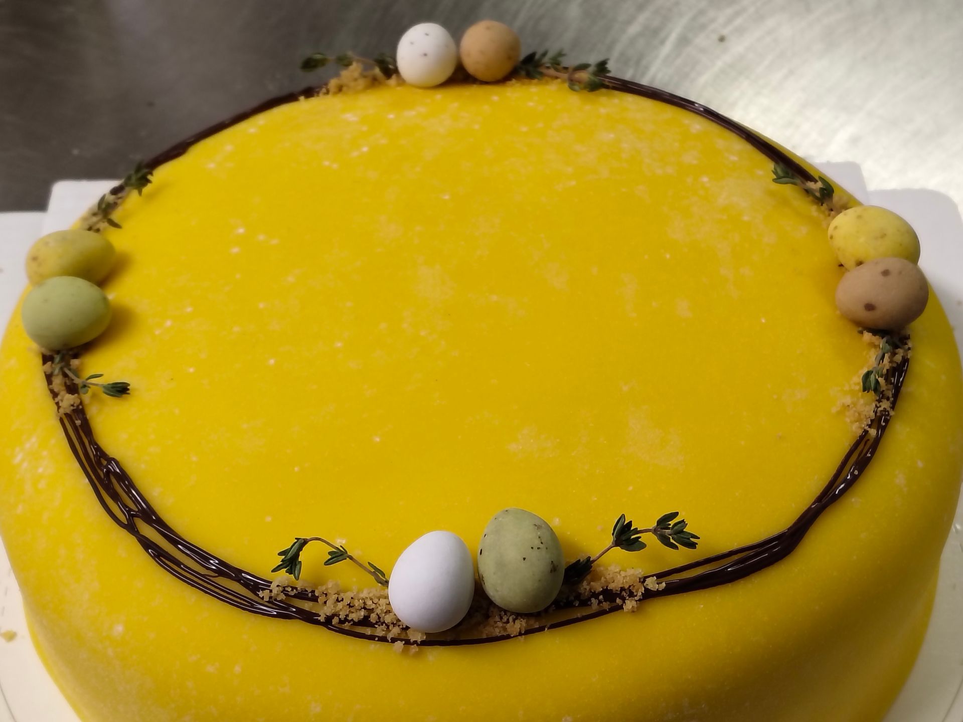 Gul rund kaka med chokladkant och små pastellfärgade ägg på toppen