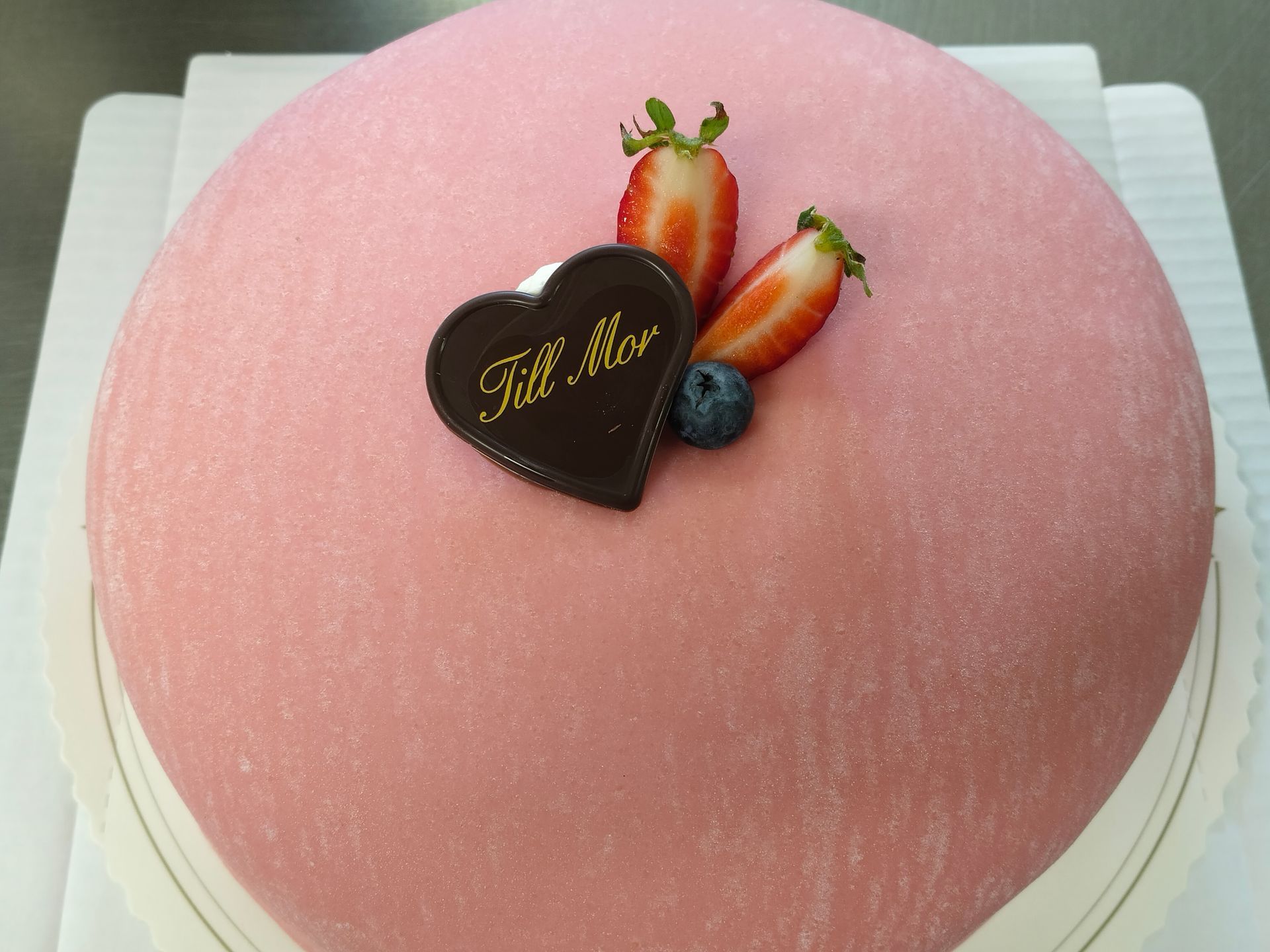 Rosa tårta med jordgubbar, blåbär och chokladhjärta på en vit tallrik