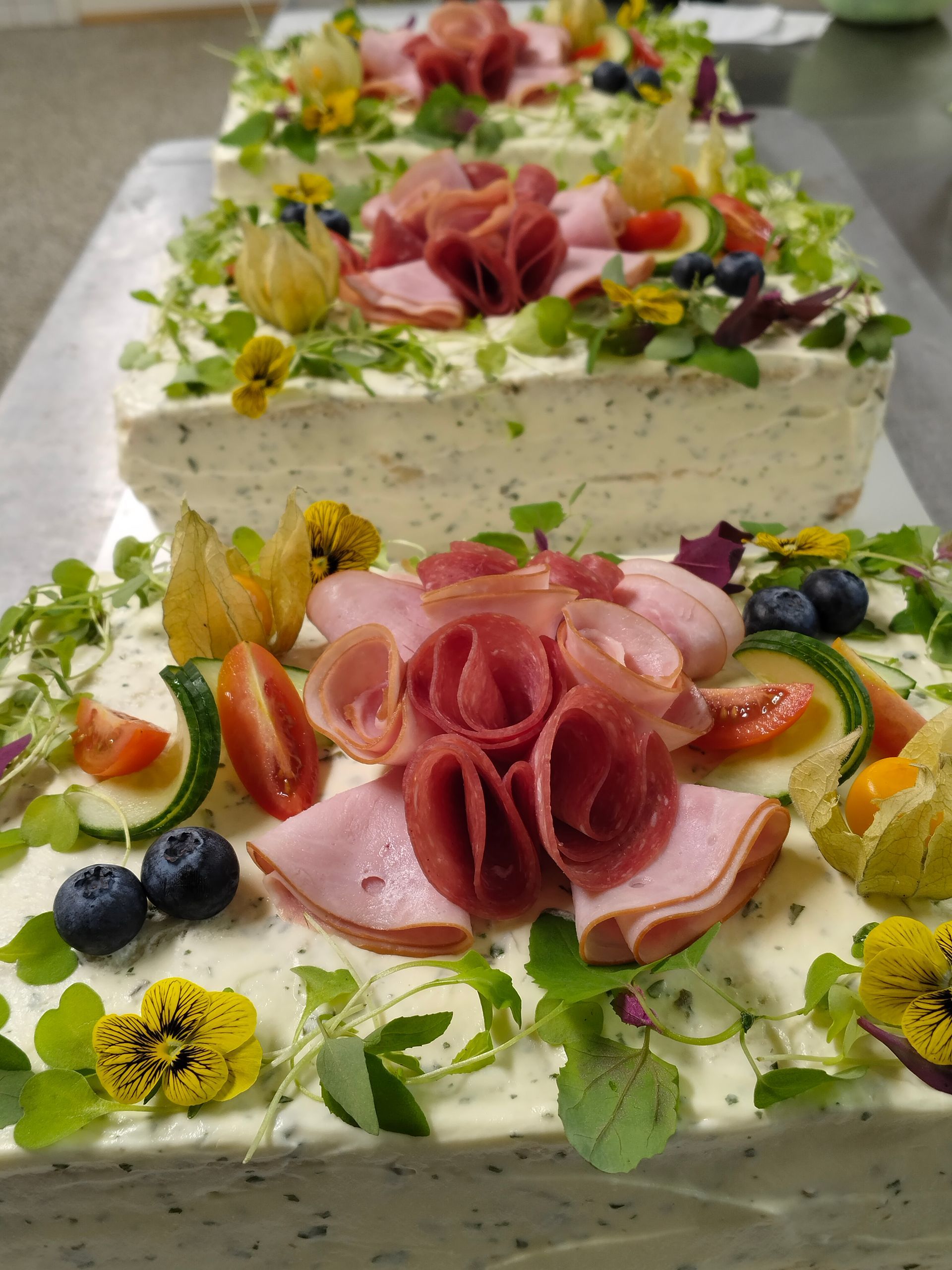 Dekorerad lagertårta med vit frosting, rosa blomliknande frostingrosor, bär och ätbara blommor