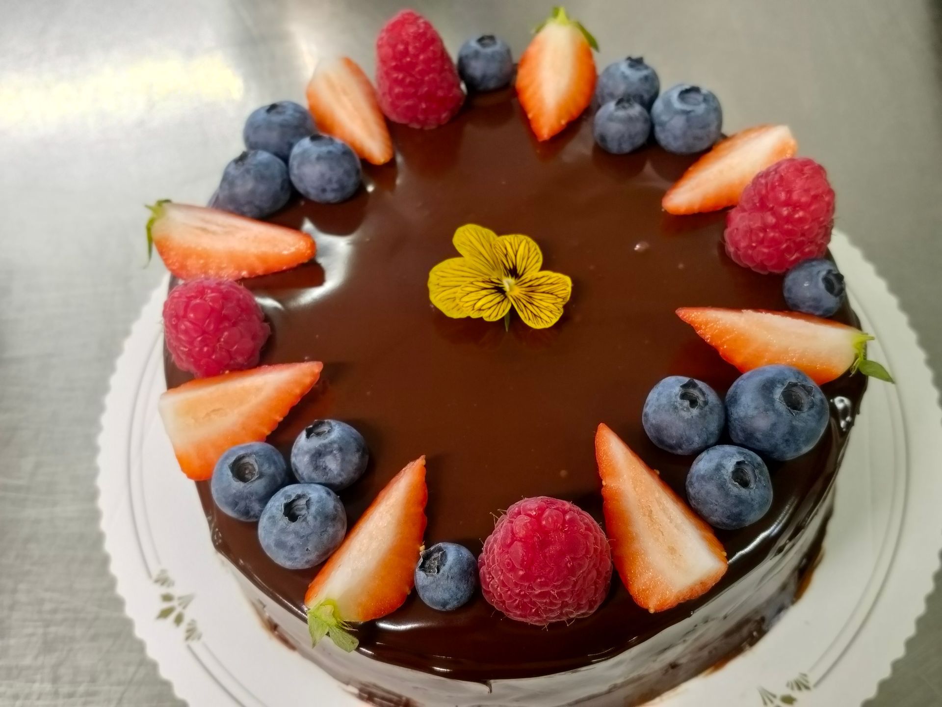 Chokladglaserad tårta toppad med jordgubbar, blåbär, hallon och en gul blomdekoration