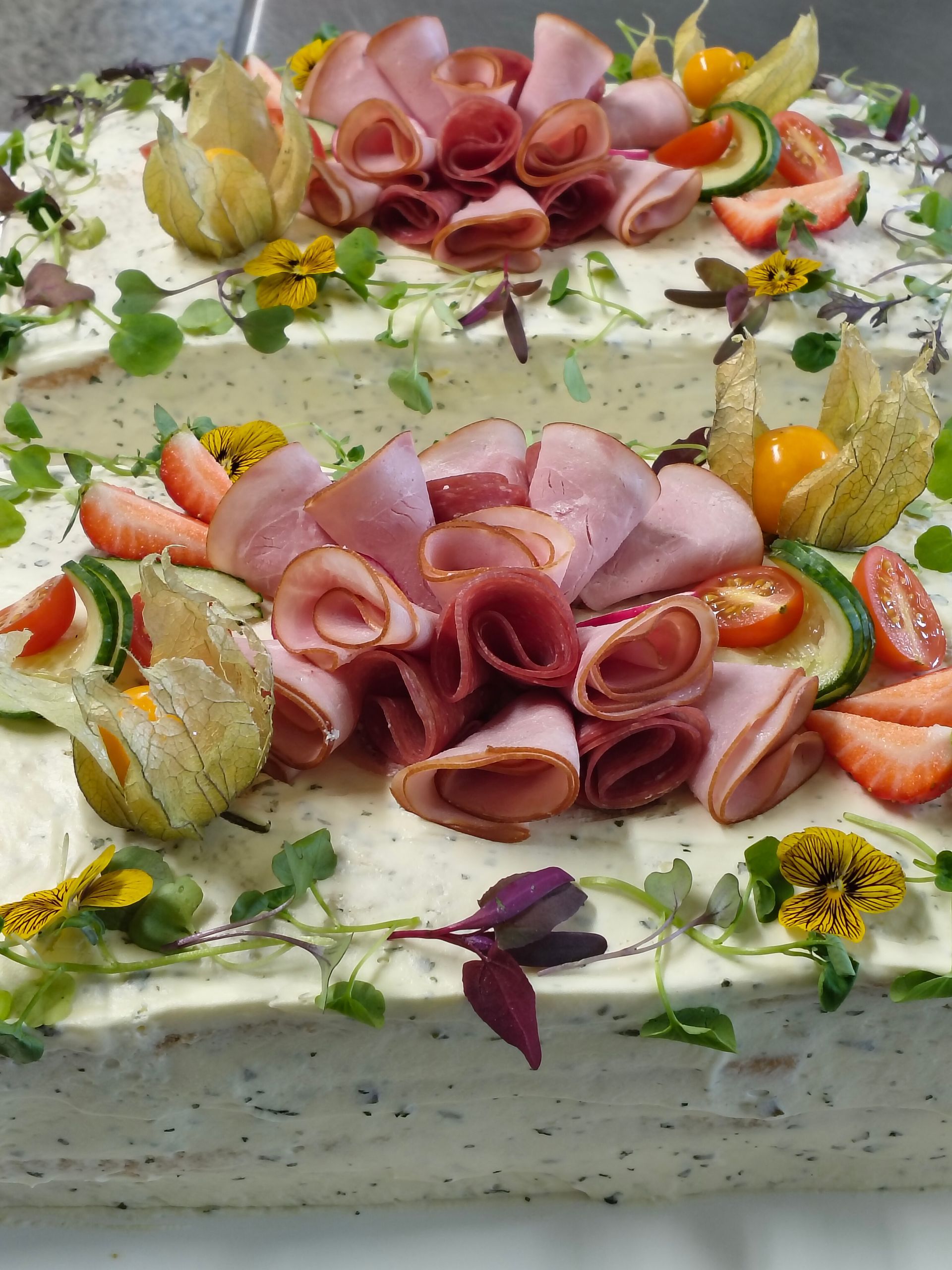 Dekorerad rektangulär tårta med vit frosting, jordgubbs- och skinkrosetter och ätbara blommor ovanpå