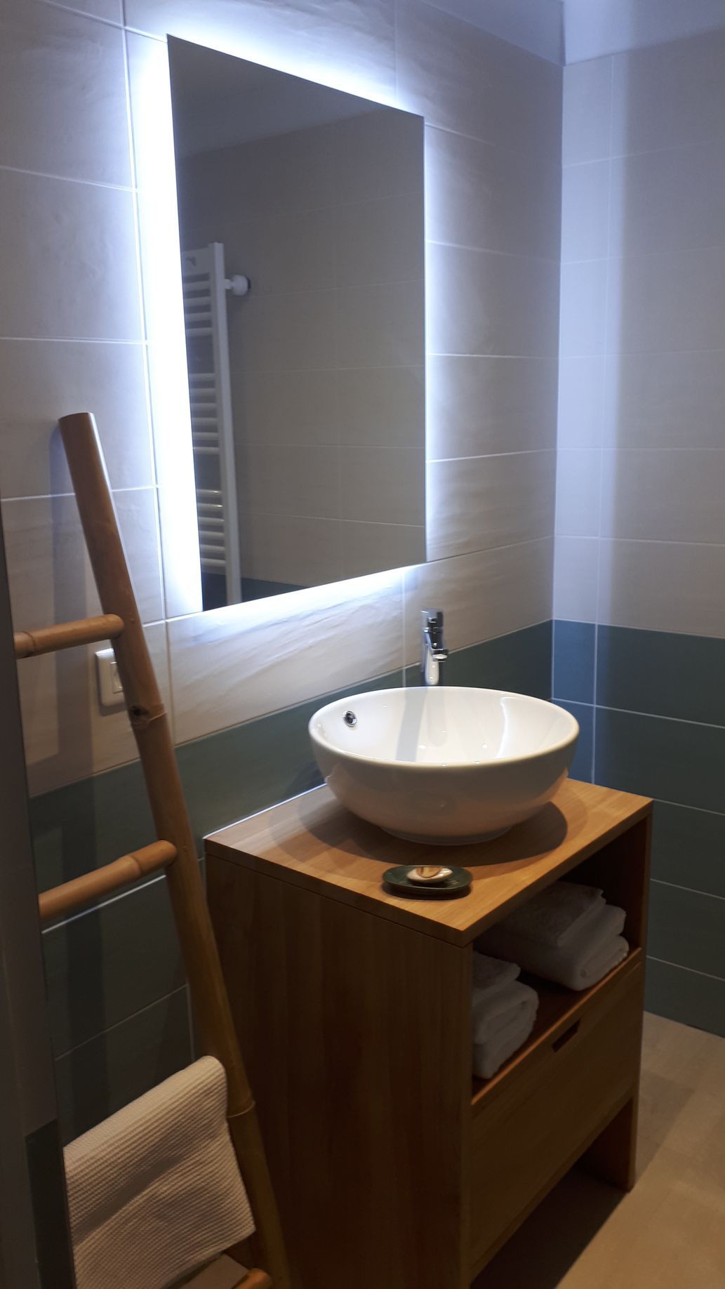 Lavabo d'une salle de bains avec miroir faisant de la lumière, une vasque et une échelle en bambou