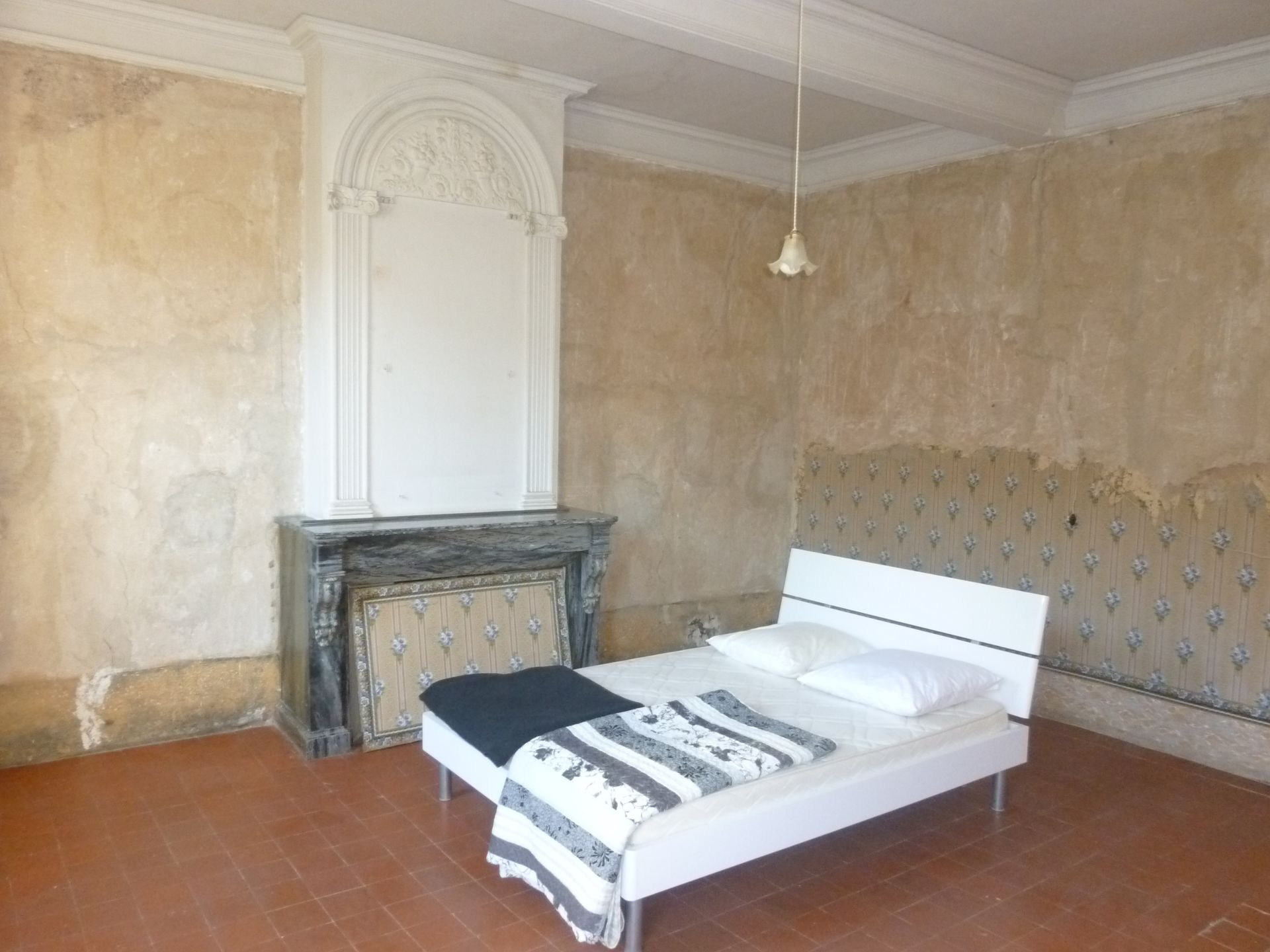 Lit au milieu d'une pièce avec une cheminée, le tout assez démodé