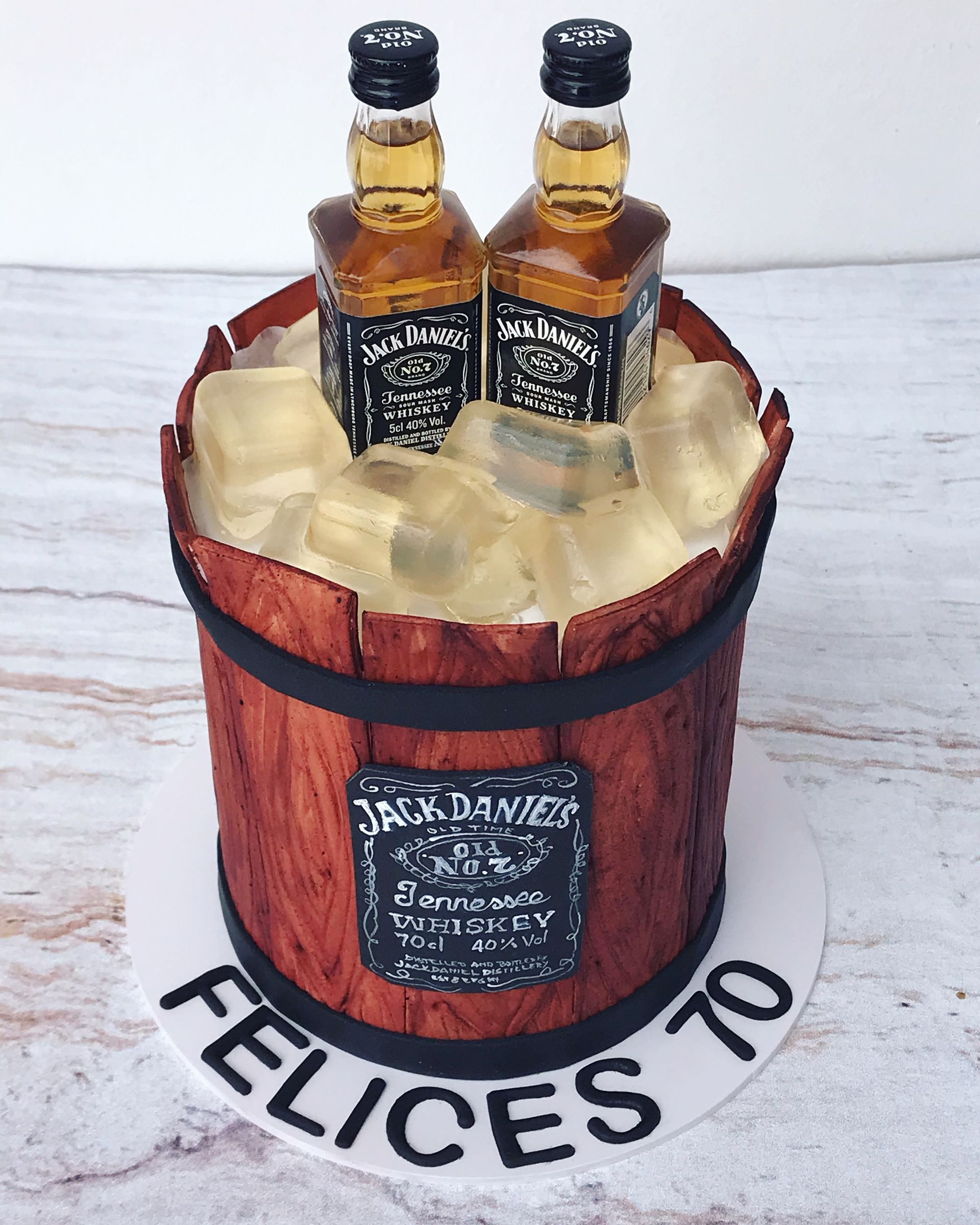 Un pastel con dos botellas de Jack Daniels en un cubo de madera.