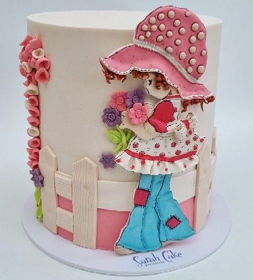 Un pastel con una niña con un sombrero rosa sosteniendo flores.