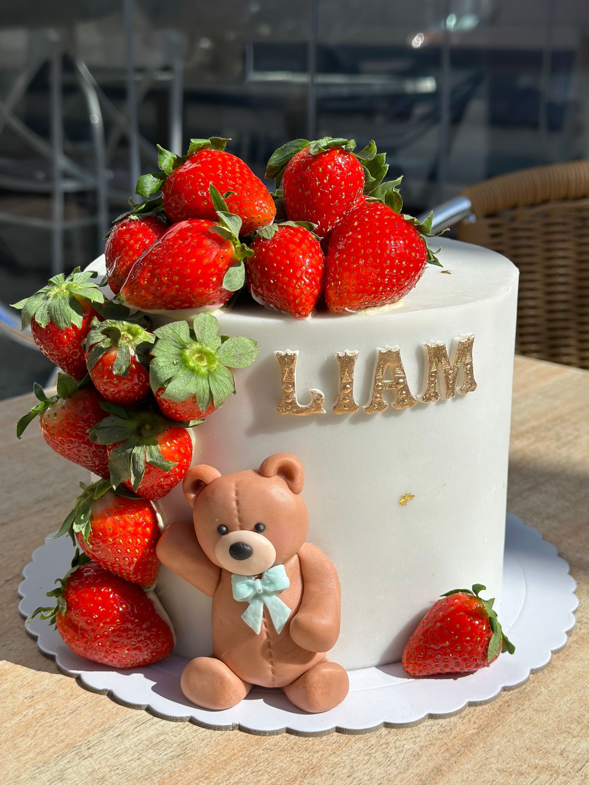 Un pastel con fresas y un osito de peluche encima.
