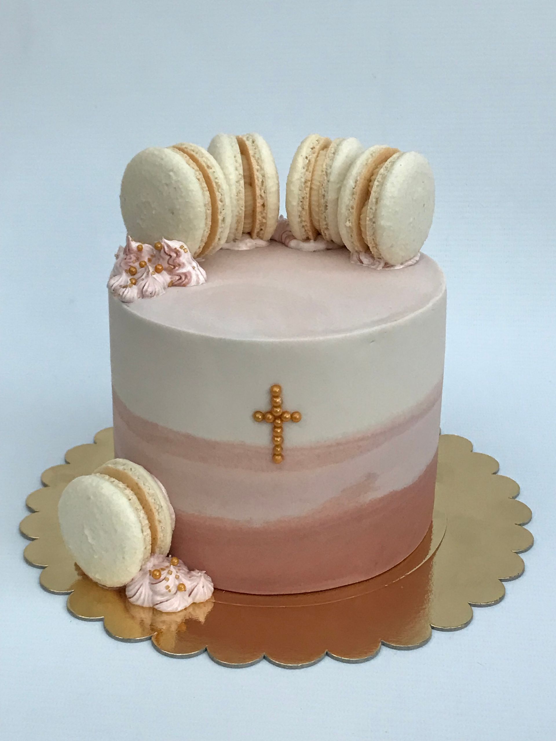 Un pastel rosa y blanco con macarons y una cruz en la parte superior.