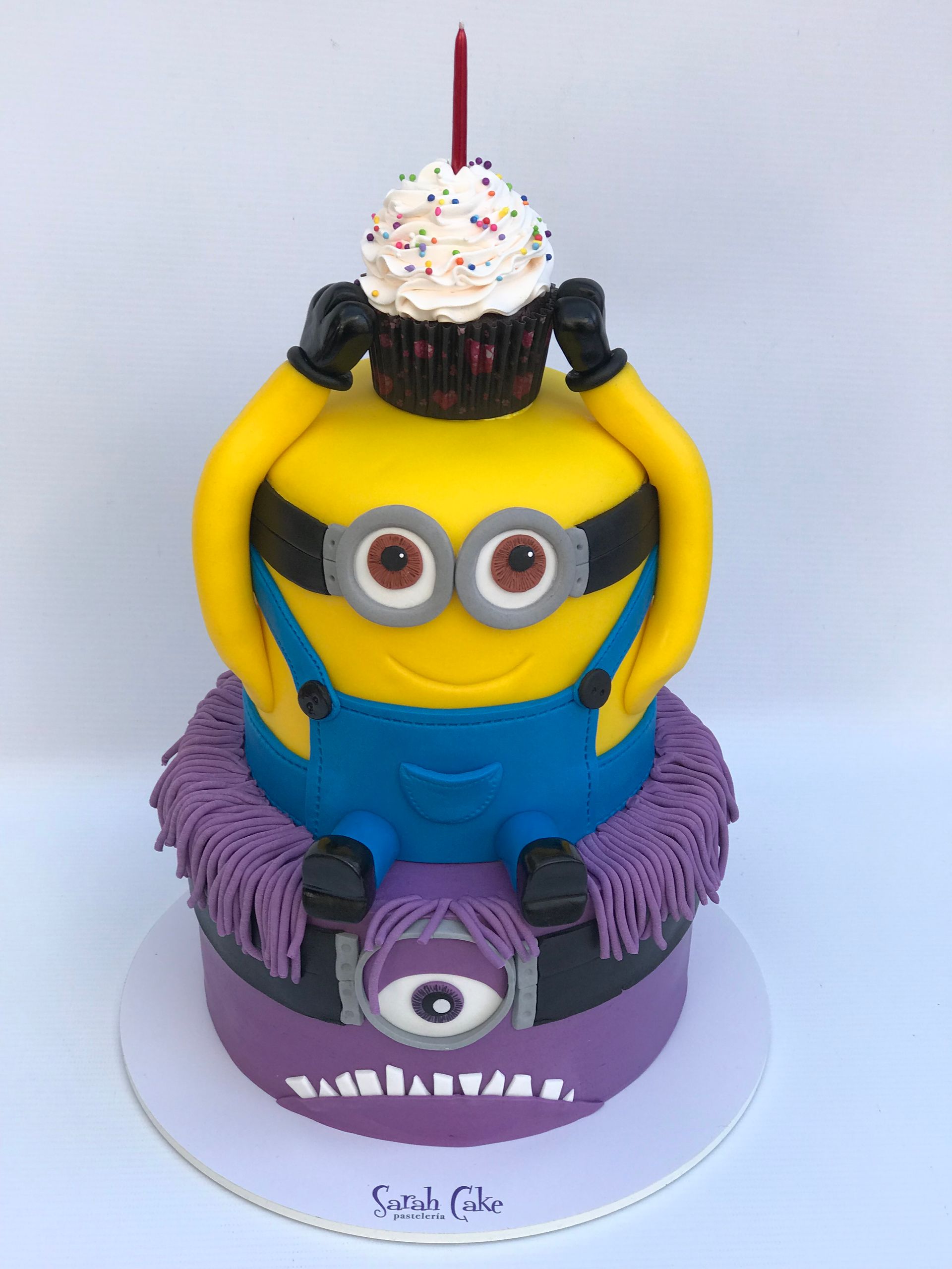 Un pastel de Minion con un cupcake encima.