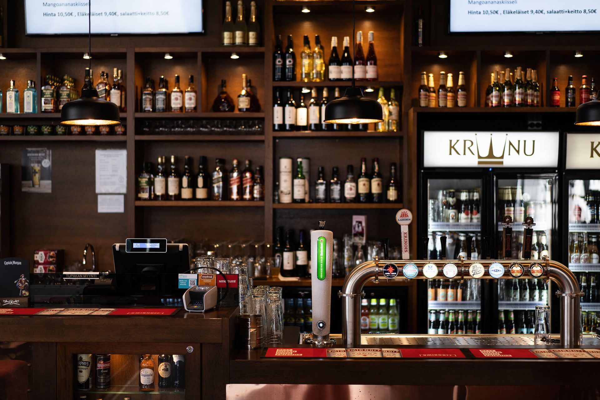 Baari, jossa on hyllyt alkoholijuomia, oluthanoja ja kahvikone kiillotetun tiskin takana.