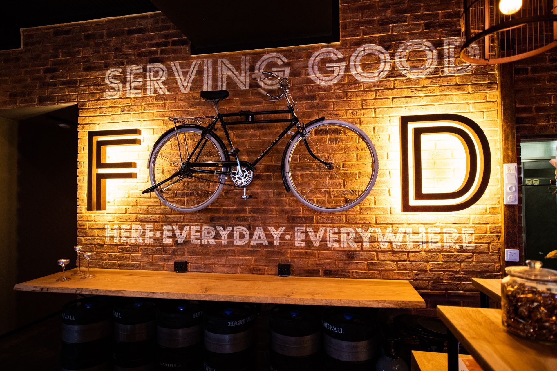 Tiiliseinäkyltti, jossa on valaistu polkupyörätaide ja sanat ”FOOD” ja ”serving coal” lämpimässä valossa
