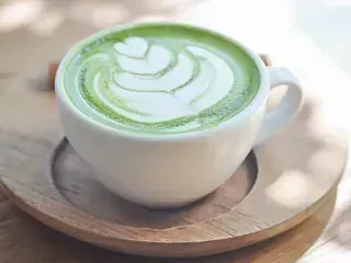 Una taza de té verde con leche en un platillo de madera sobre una mesa de madera.