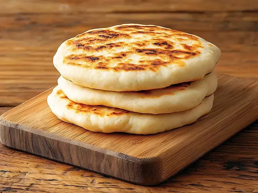 Se apilan tres arepas una encima de otra sobre una tabla de cortar de madera.