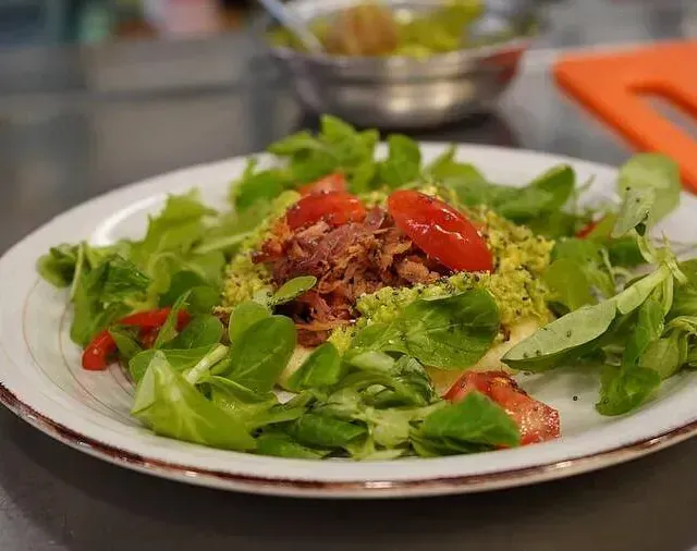 Un plato blanco cubierto con una ensalada de lechuga, tomates y carne.