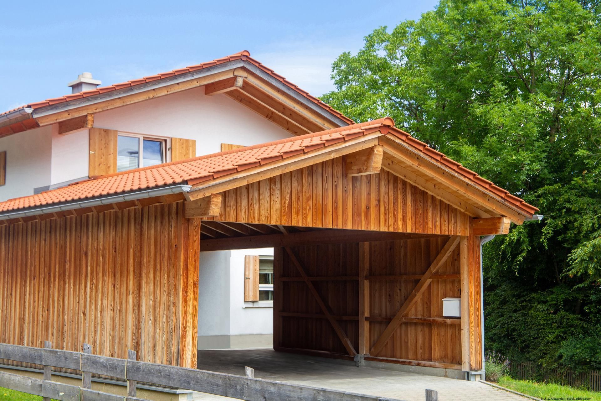 Holzcarport mit Satteldach neben einem Wohnhaus in moderner Bauweise