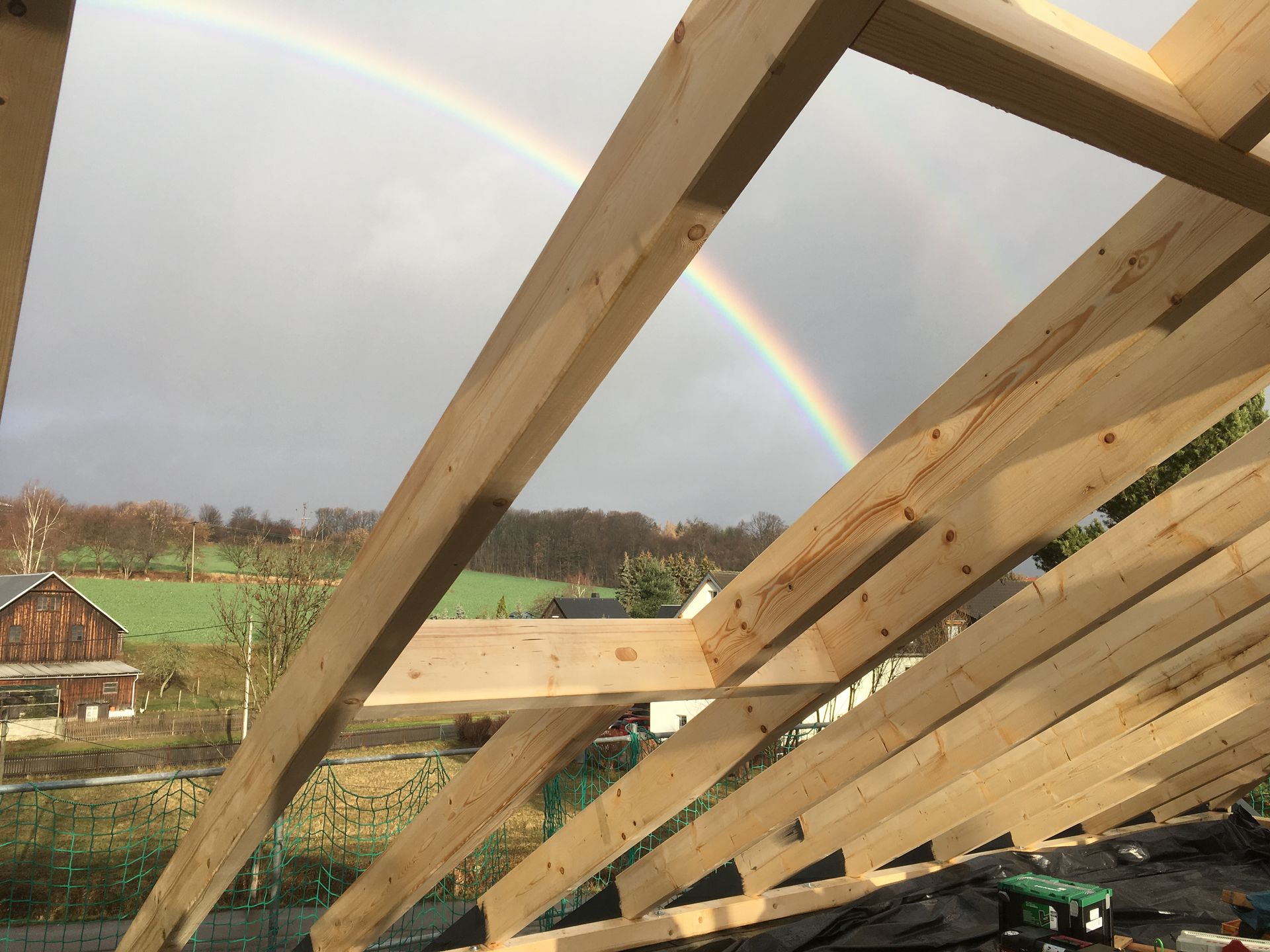 Dachkonstruktion aus Holz mit sichtbaren Sparren und Regenbogen im Hintergrund