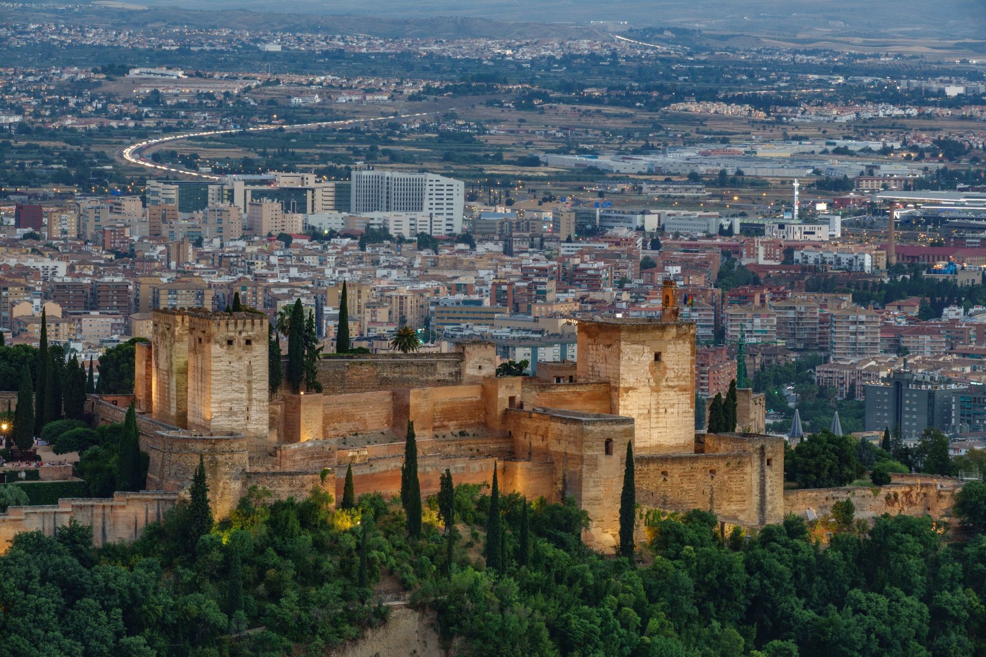 La fortaleza de la Alhambra en Granada, España, iluminada al anochecer con las luces de la ciudad como telón de fondo.