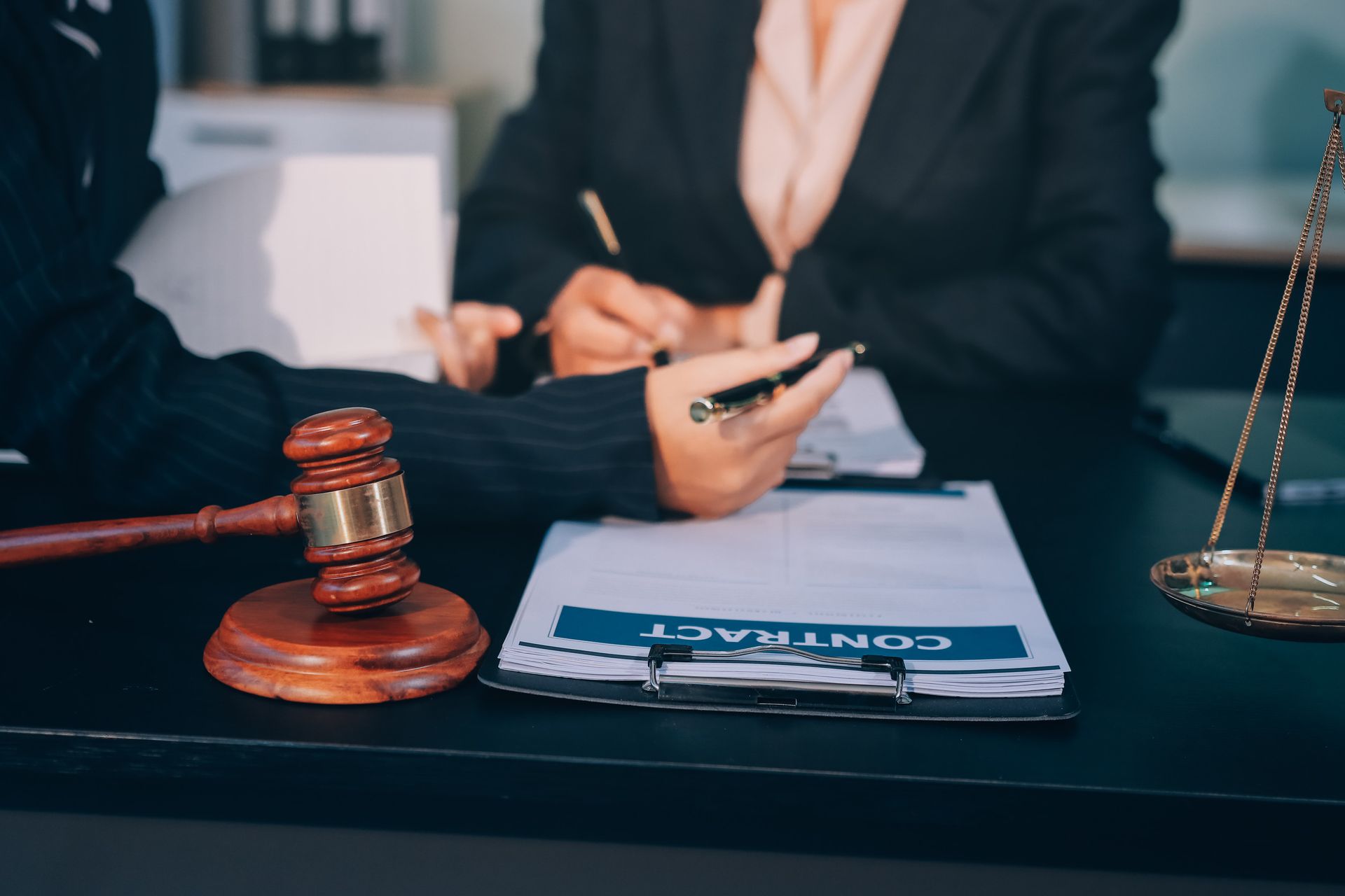 Primer plano de un entorno legal con un mazo, una balanza y dos personas revisando un contrato. Una persona firma.