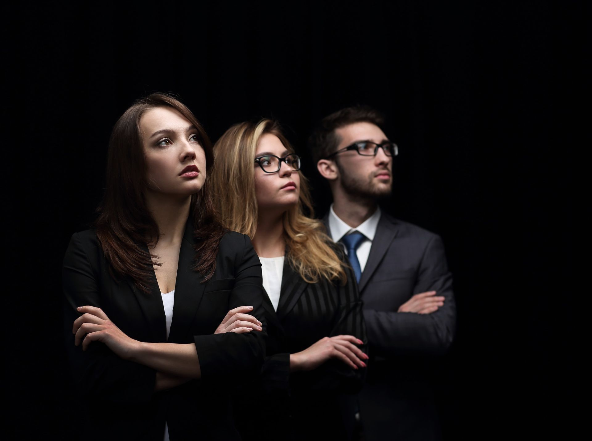 Tres profesionales de negocios mirando hacia arriba, con los brazos cruzados, sobre un fondo negro.