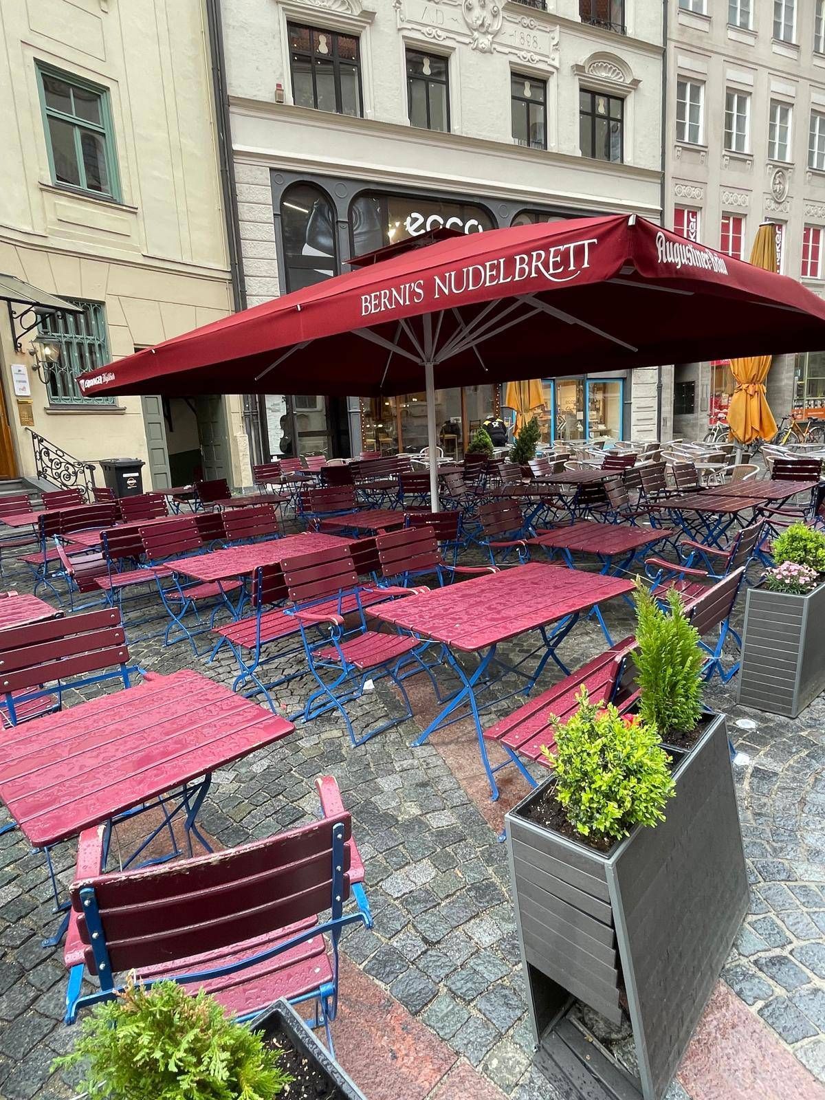 Eine Reihe von Tischen und Stühlen unter einem Sonnenschirm vor dem Ristorante Berni's Nudelbrett