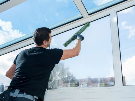 Une personne de dos nettoie de grandes vitres.