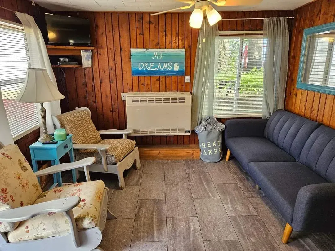 Cozy wood-paneled living room with blue sofa, white chairs, woven rug, and “DREAMS” wall sign