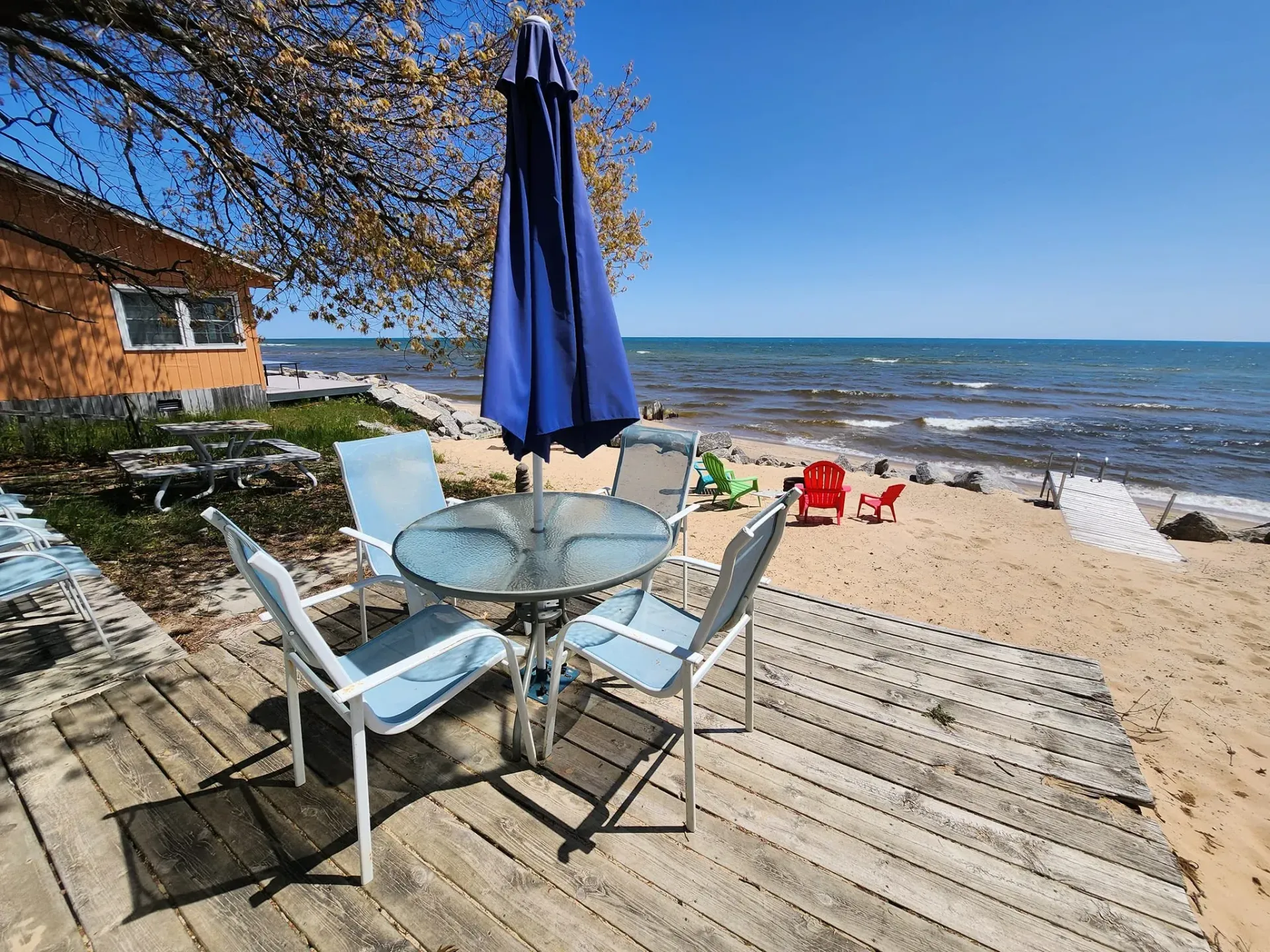 Patio deck with glass table, blue umbrella, chairs, and beach view by the water