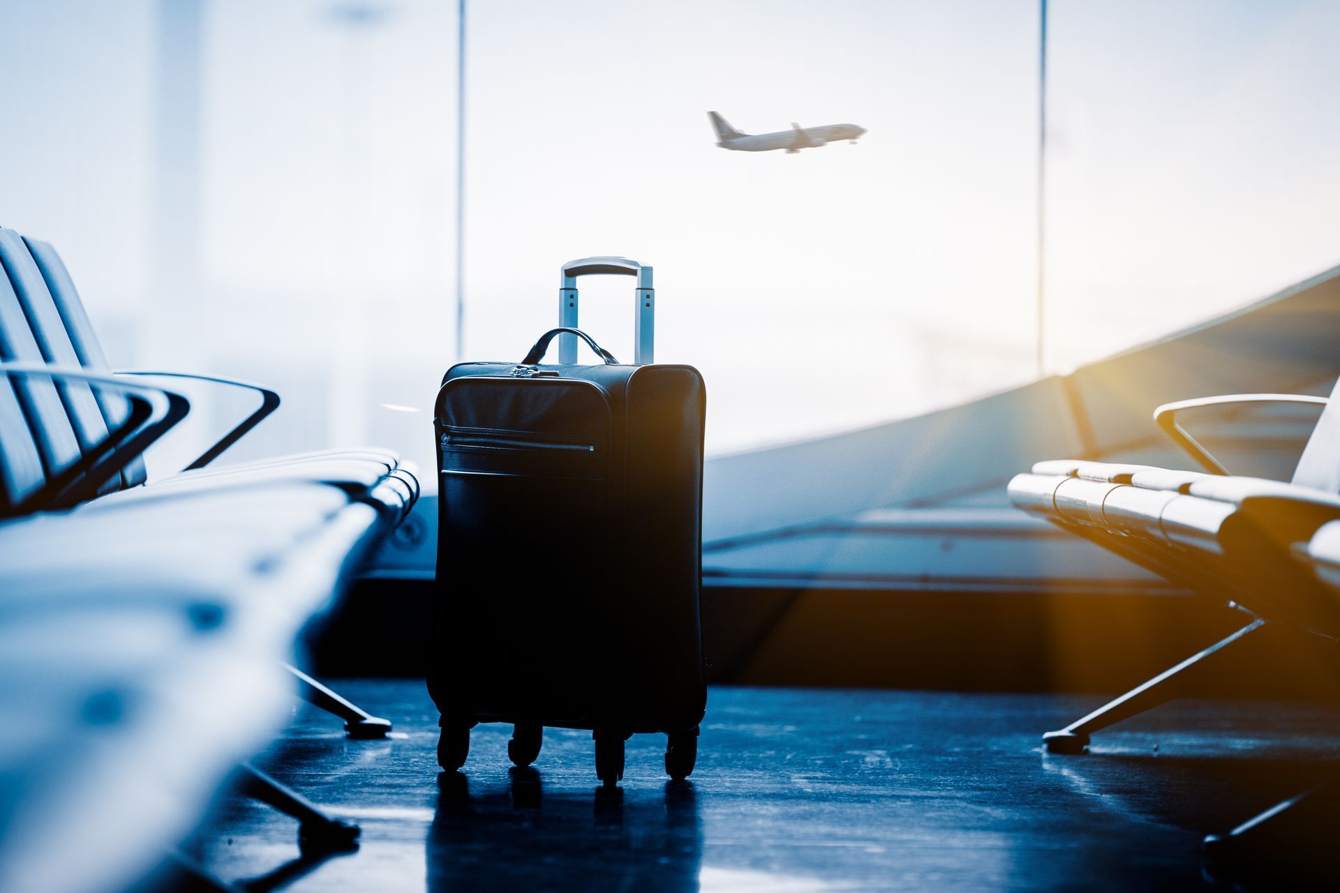 Valise dans la salle d'attente de l'aéroport, un avion visible par la fenêtre est en train de décoller.