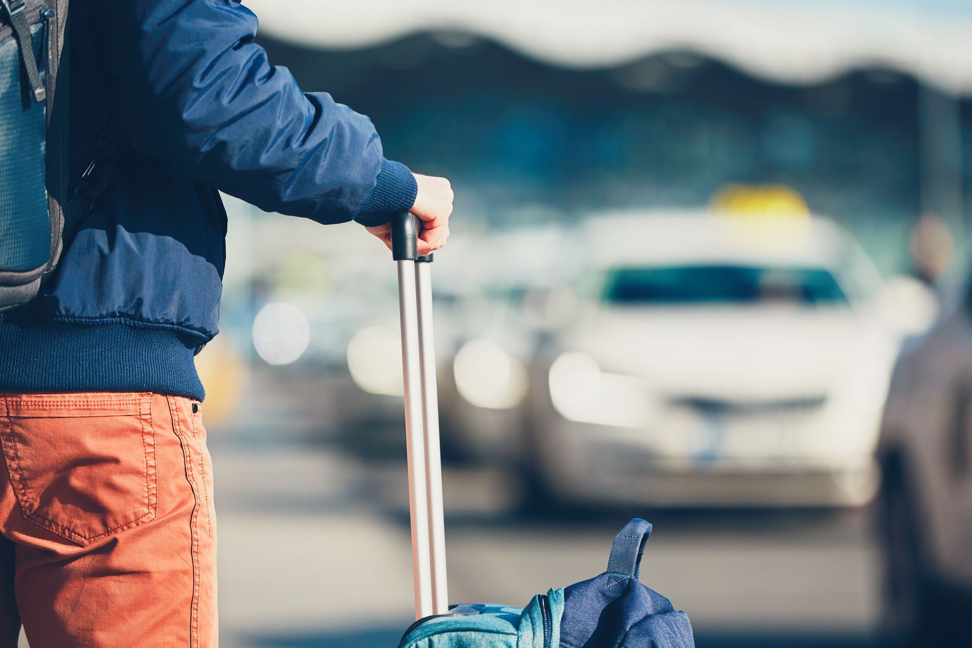 Voyageur en veste bleue tirant une valise dans une rue avec des voitures en arrière-plan.