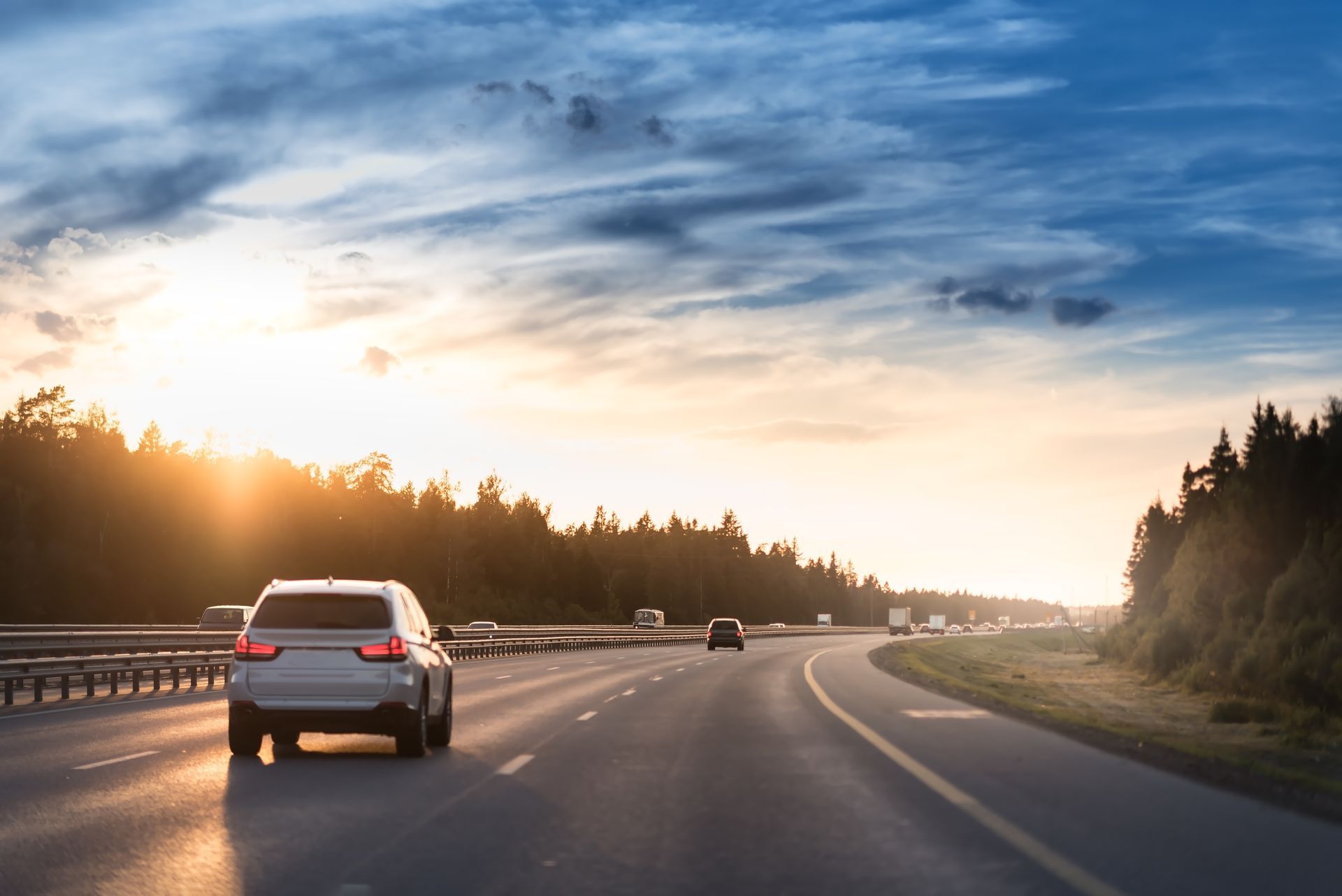 Voitures roulant sur une autoroute sinueuse au coucher du soleil, sous un ciel nuageux.