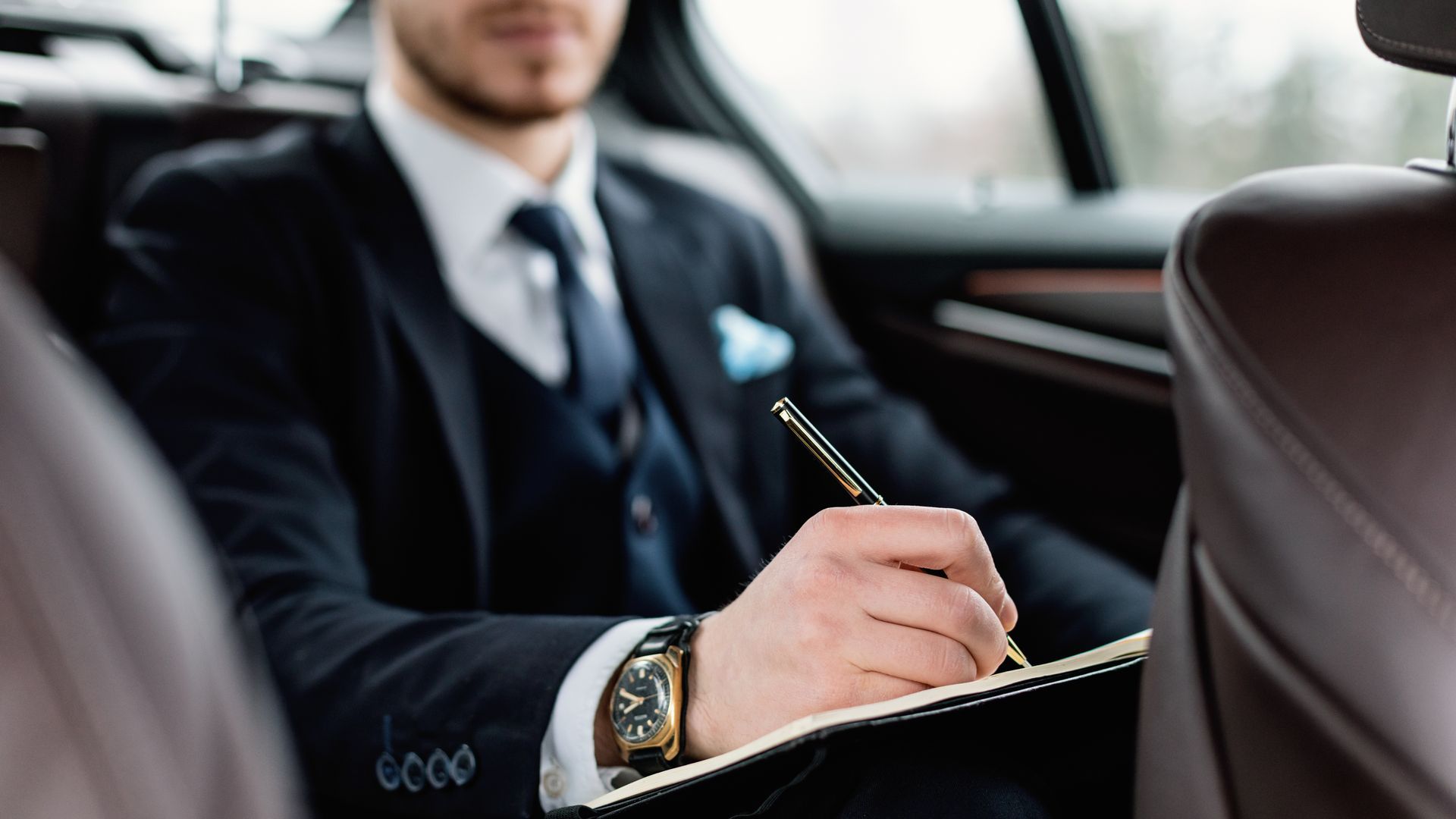 Un homme d'affaires écrit sur la banquette arrière d'une voiture, vêtu d'un costume sombre et portant une montre.