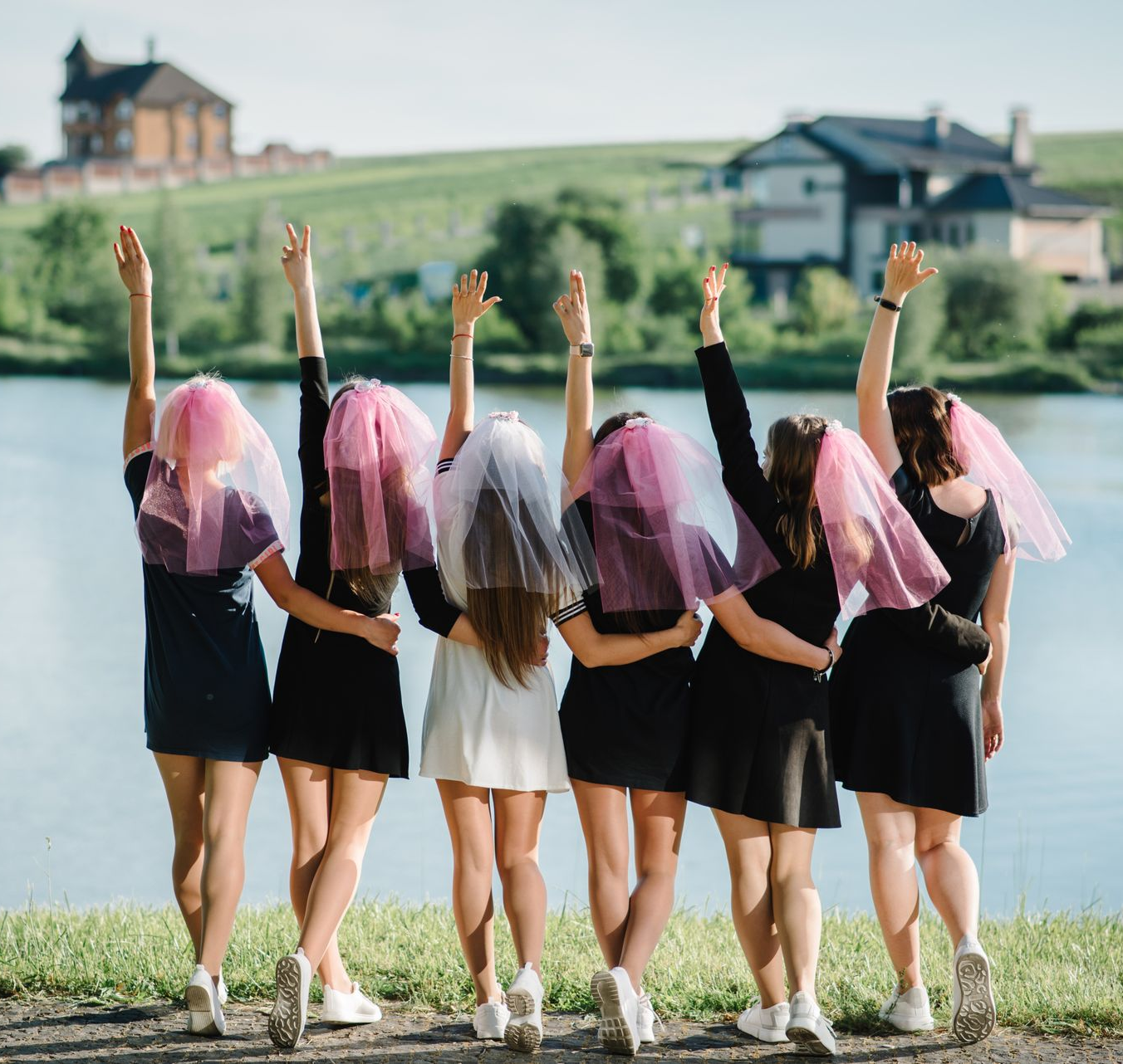 Six femmes de dos portant des voiles aux couleurs vives dans les cheveux font un enterrement de vie de jeune fille au bord d'un lac.