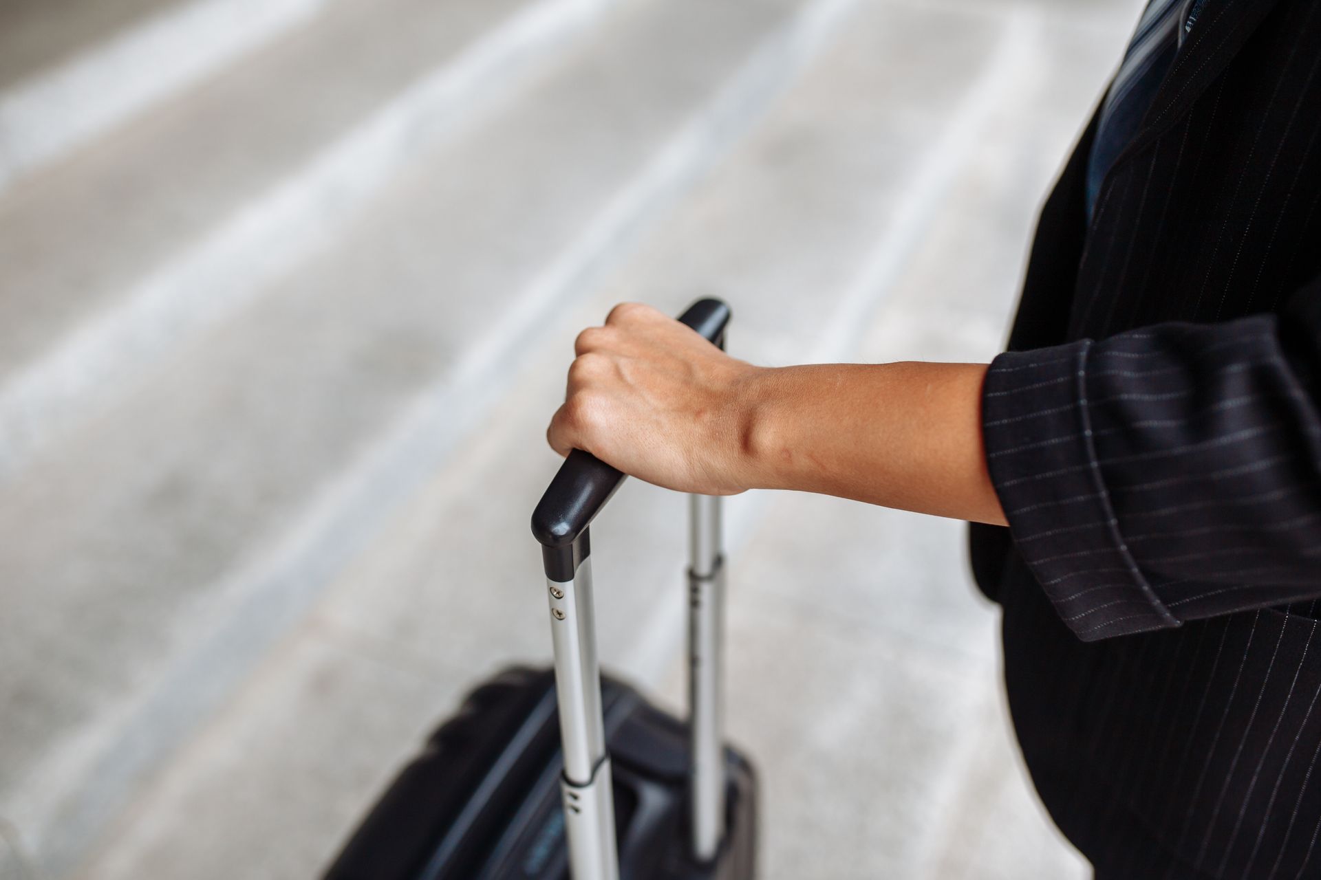 Une main agrippant la poignée d'une valise sur un trottoir.