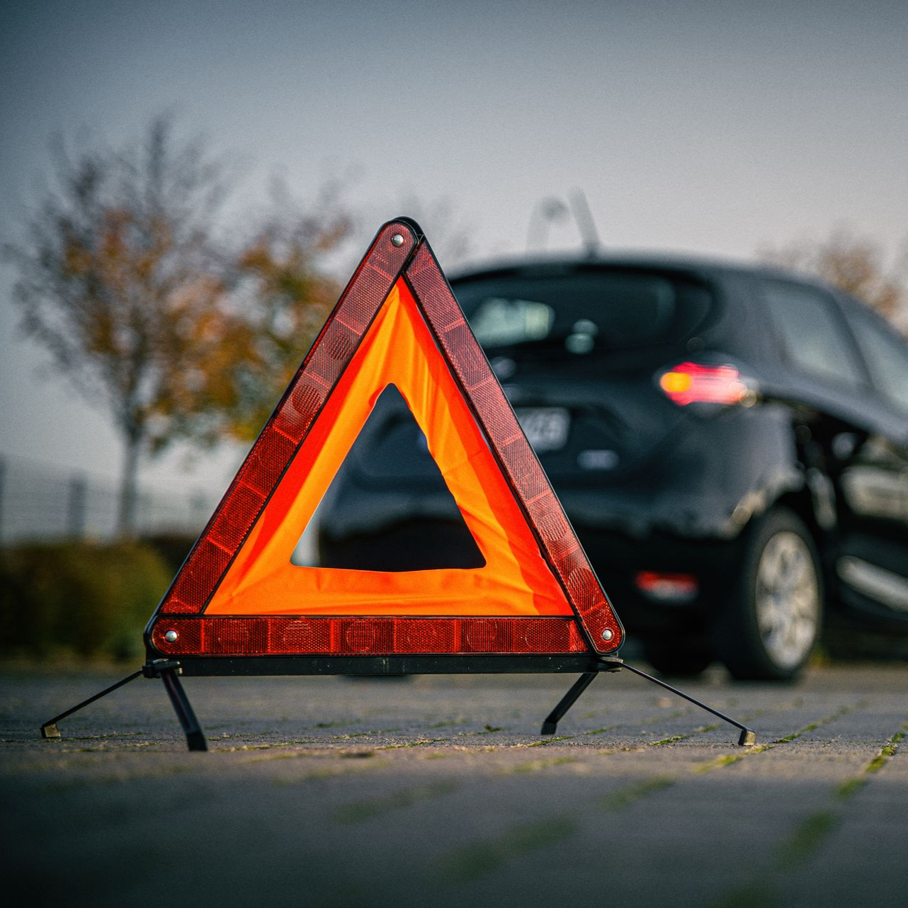 Triangle de signalisation rouge en bord de route à côté d'une voiture noire floue.