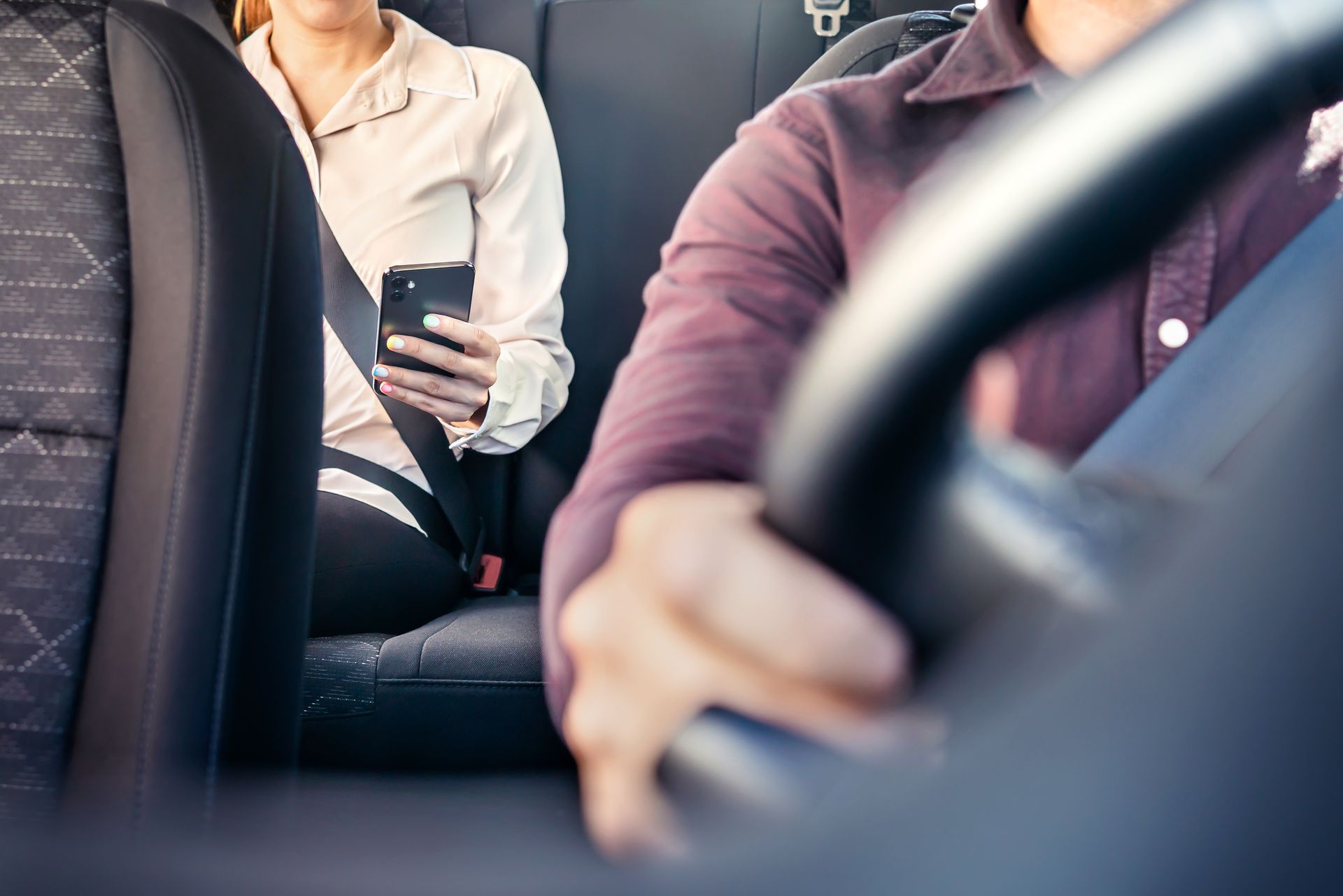 Une personne dans une voiture tient un téléphone tandis qu'une autre conduit, le volant est au premier plan.