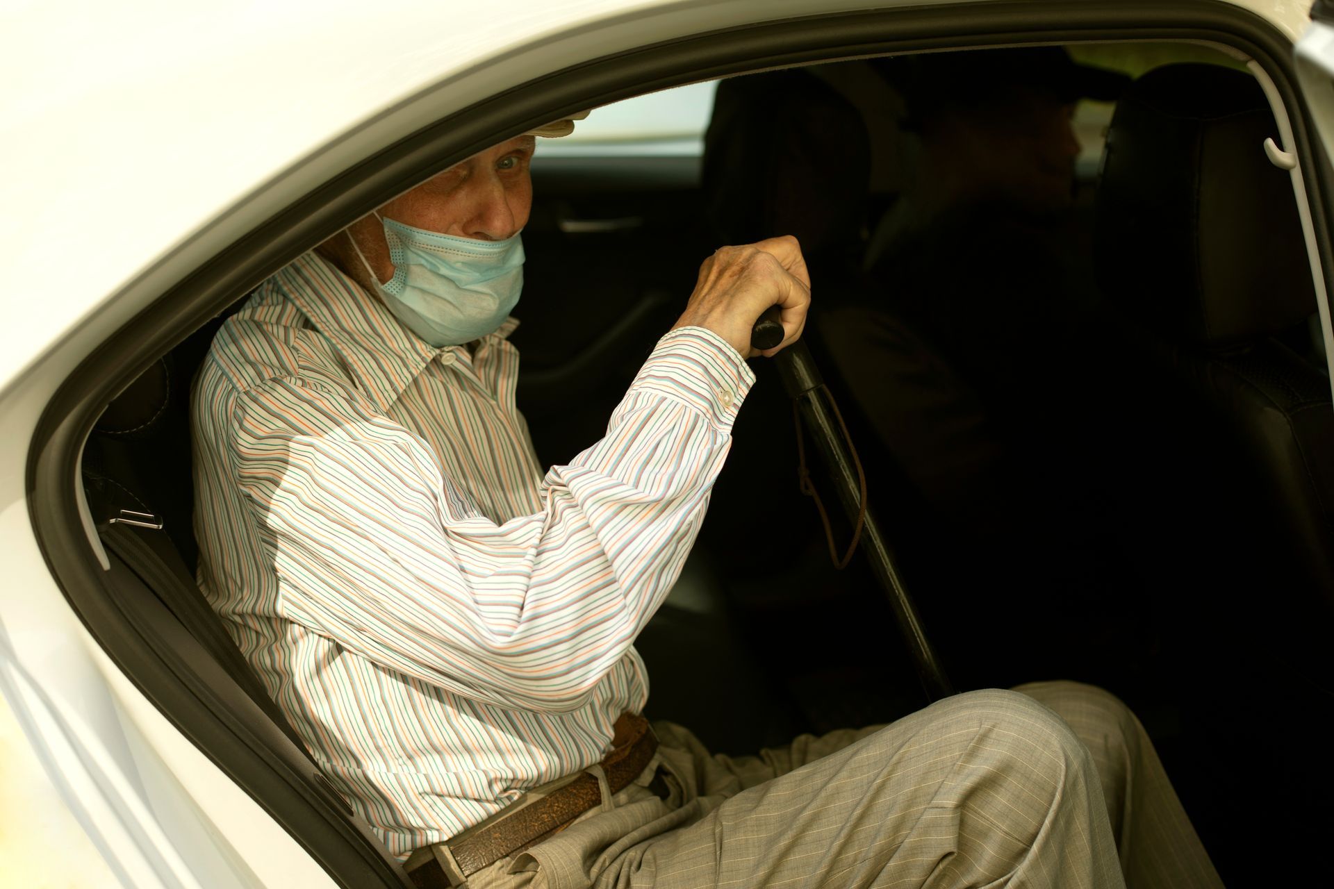 Passager masqué assis dans une voiture, tenant la poignée du siège à l'intérieur du siège arrière.