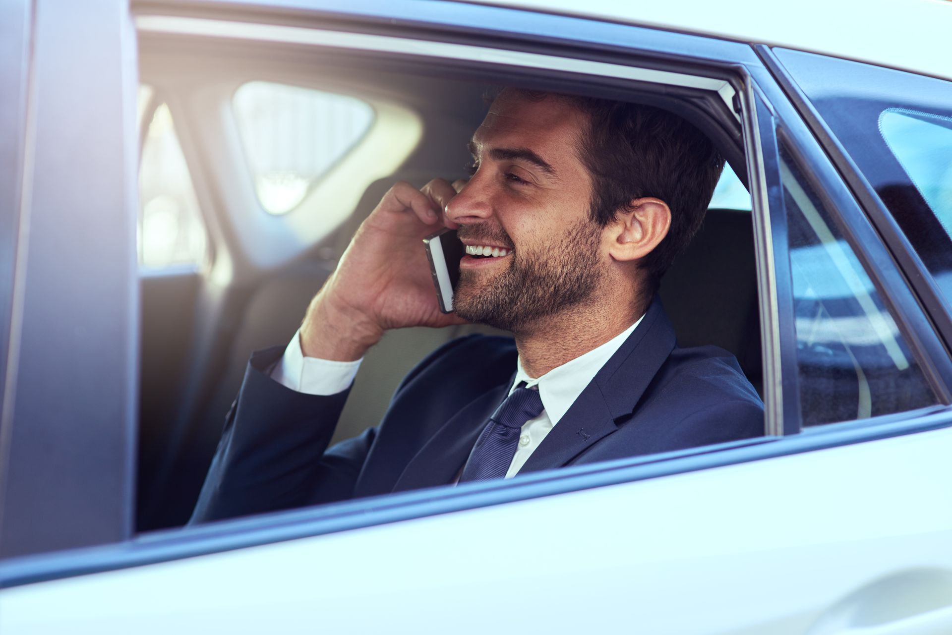 Un homme en costume sourit en parlant au téléphone à l'arrirèe d'un taxi.