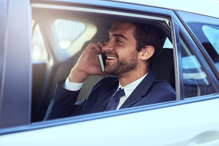 Un homme en costume sourit en parlant au téléphone dans une voiture.