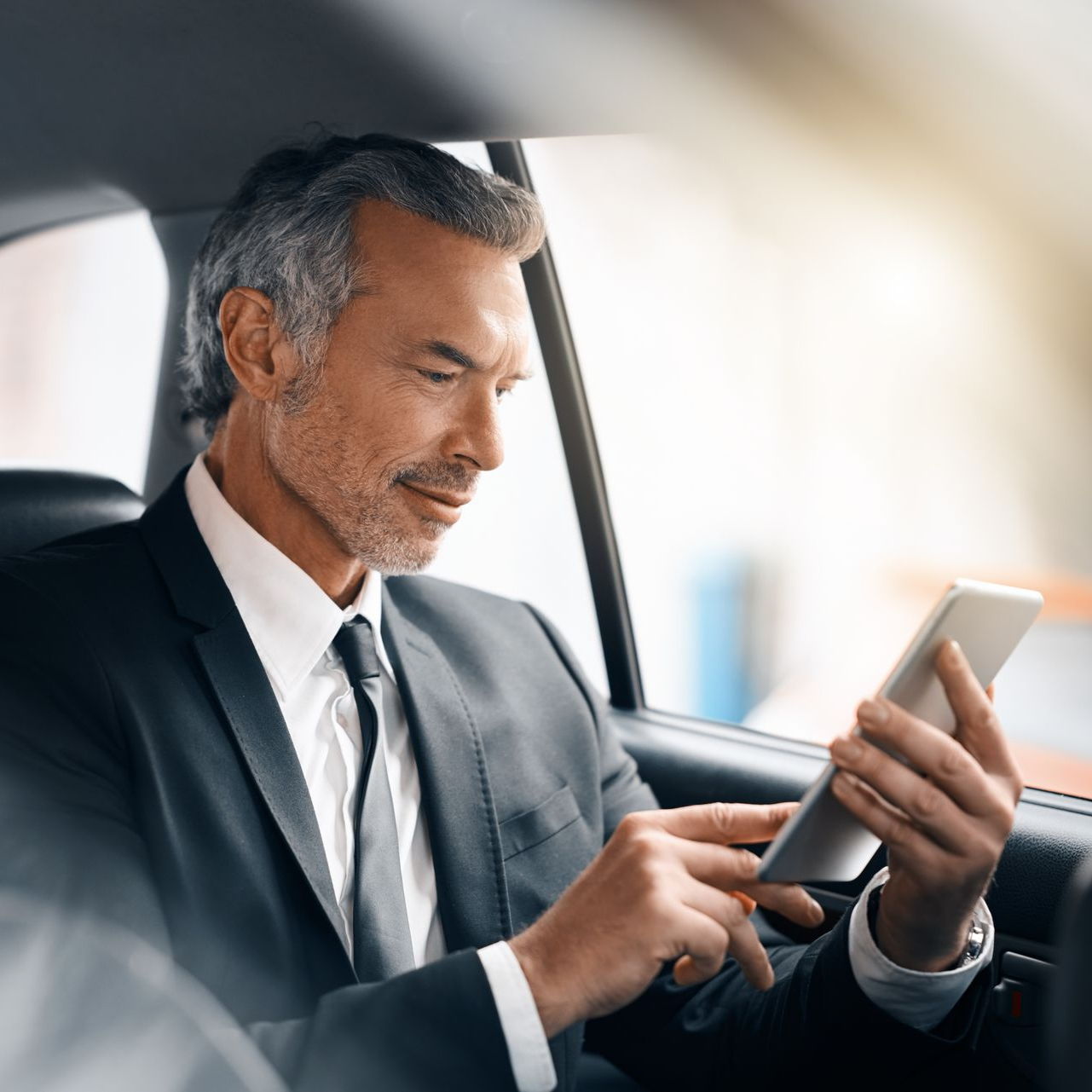 Un homme en costume sombre utilise un smartphone sur la banquette arrière d'une voiture.