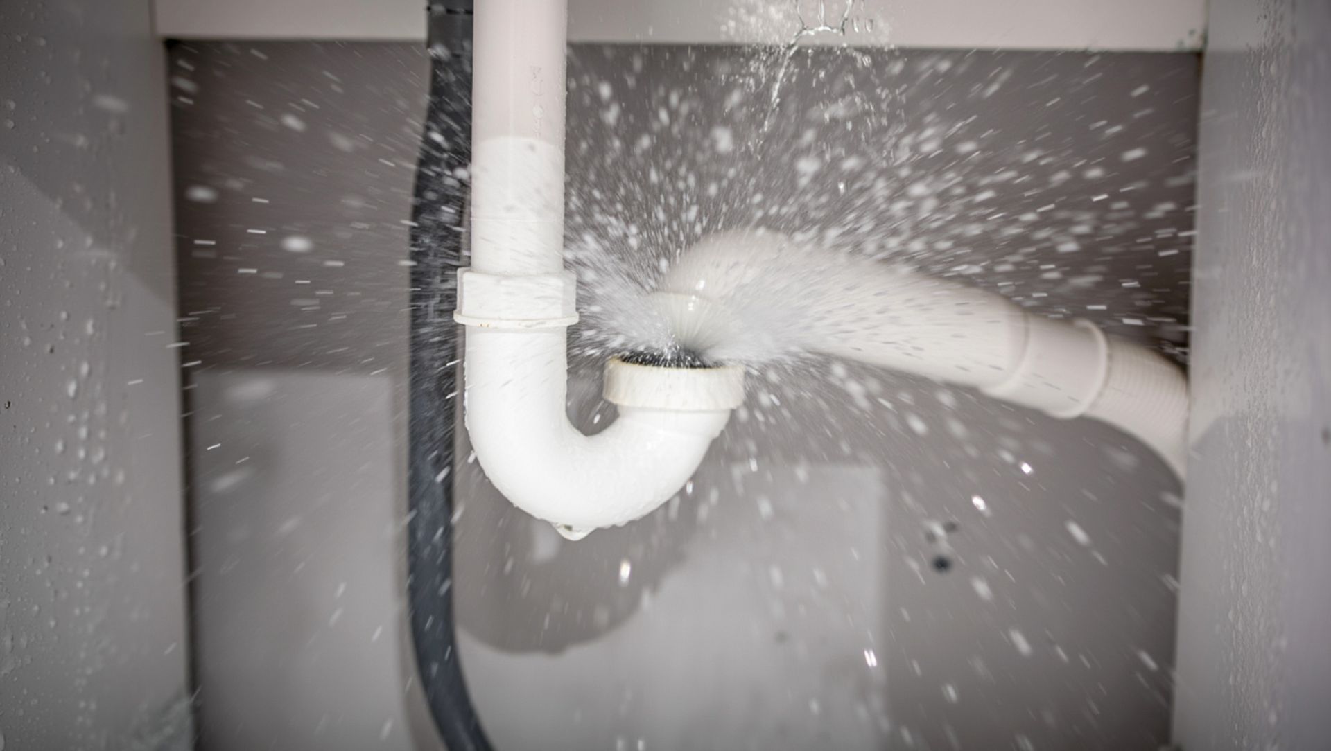 Un siphon blanc sous un évier, d'où jaillit violemment de l'eau.