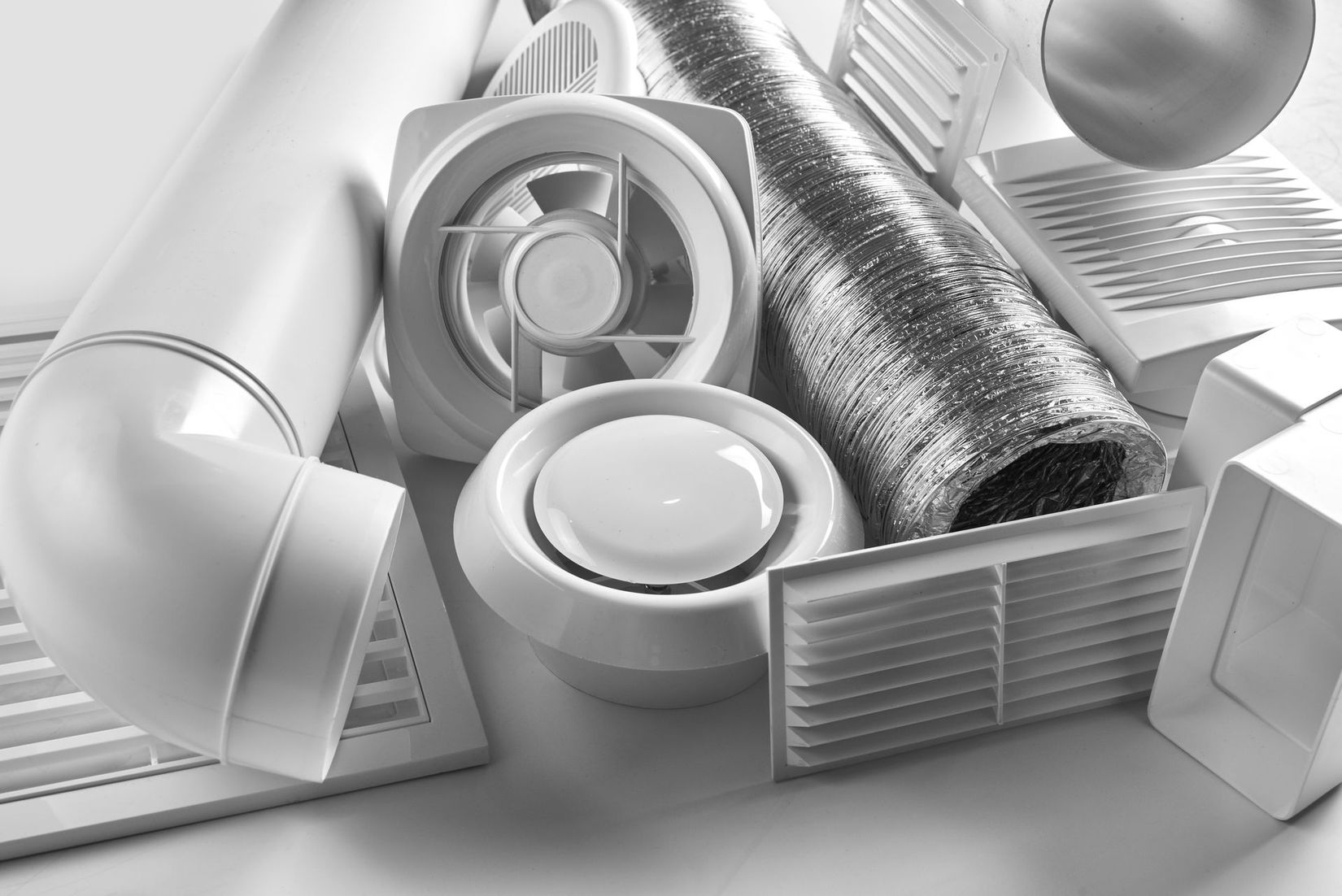 Un ensemble de composants de ventilation blancs, comprenant des conduits en plastique, un ventilateur circulaire, des grilles d'aération et des tubes flexibles.
